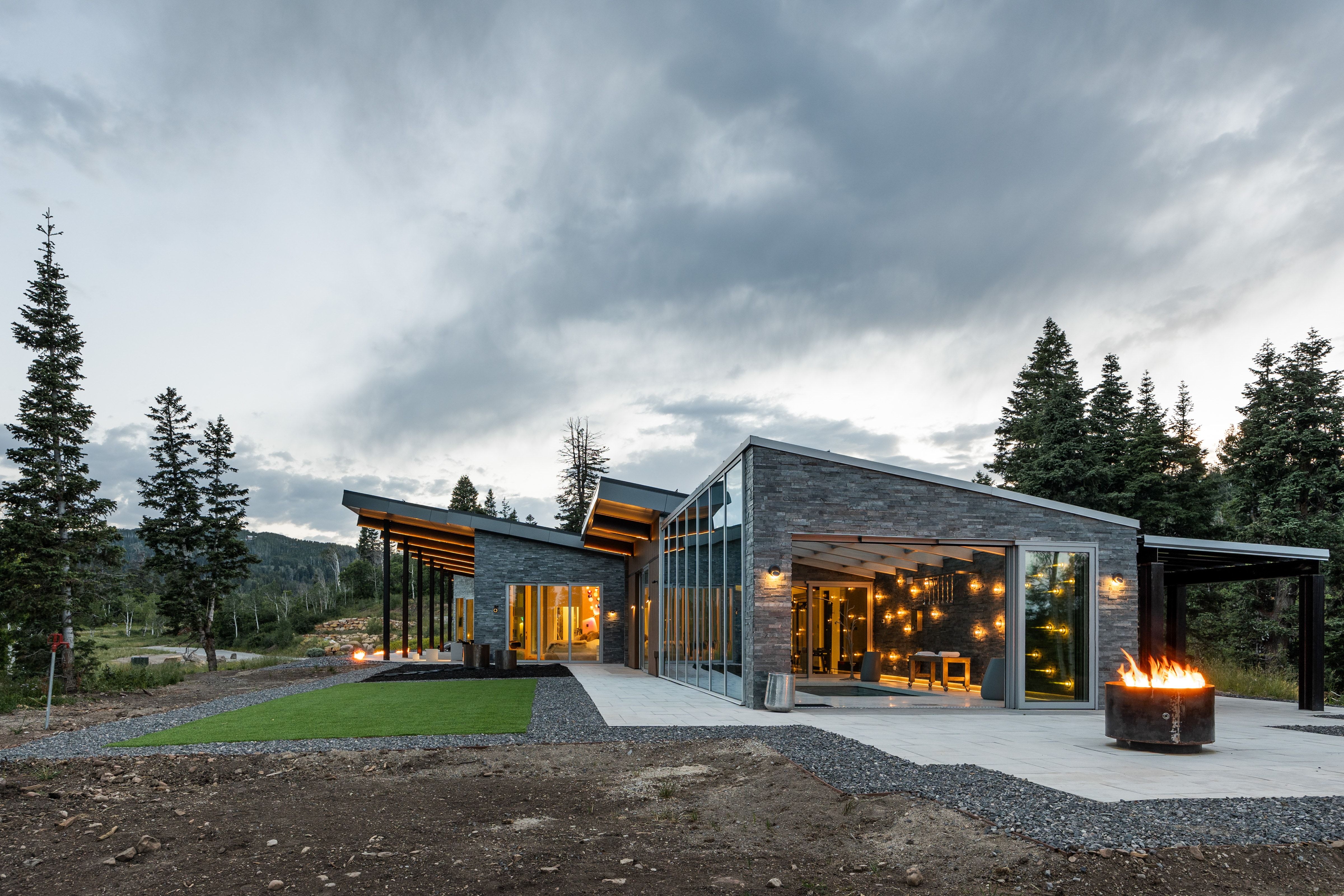 Contemporary architectural design featuring stone facade, extensive glazing, a pitched roofline, and an integrated outdoor patio with a fire pit