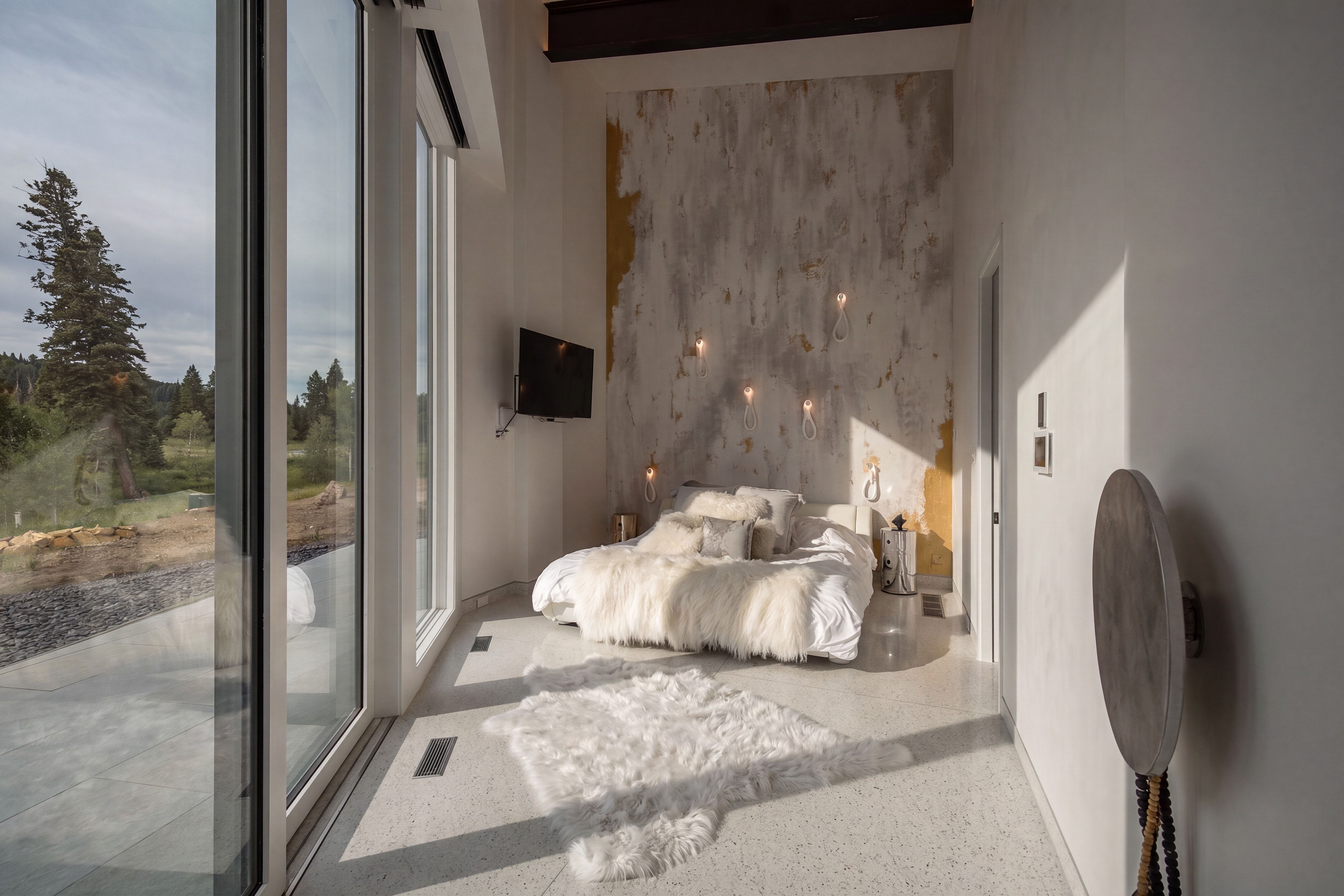 Floor-to-ceiling glass paneling, a textured accent wall with embedded sconce lighting, and light-toned terrazzo flooring