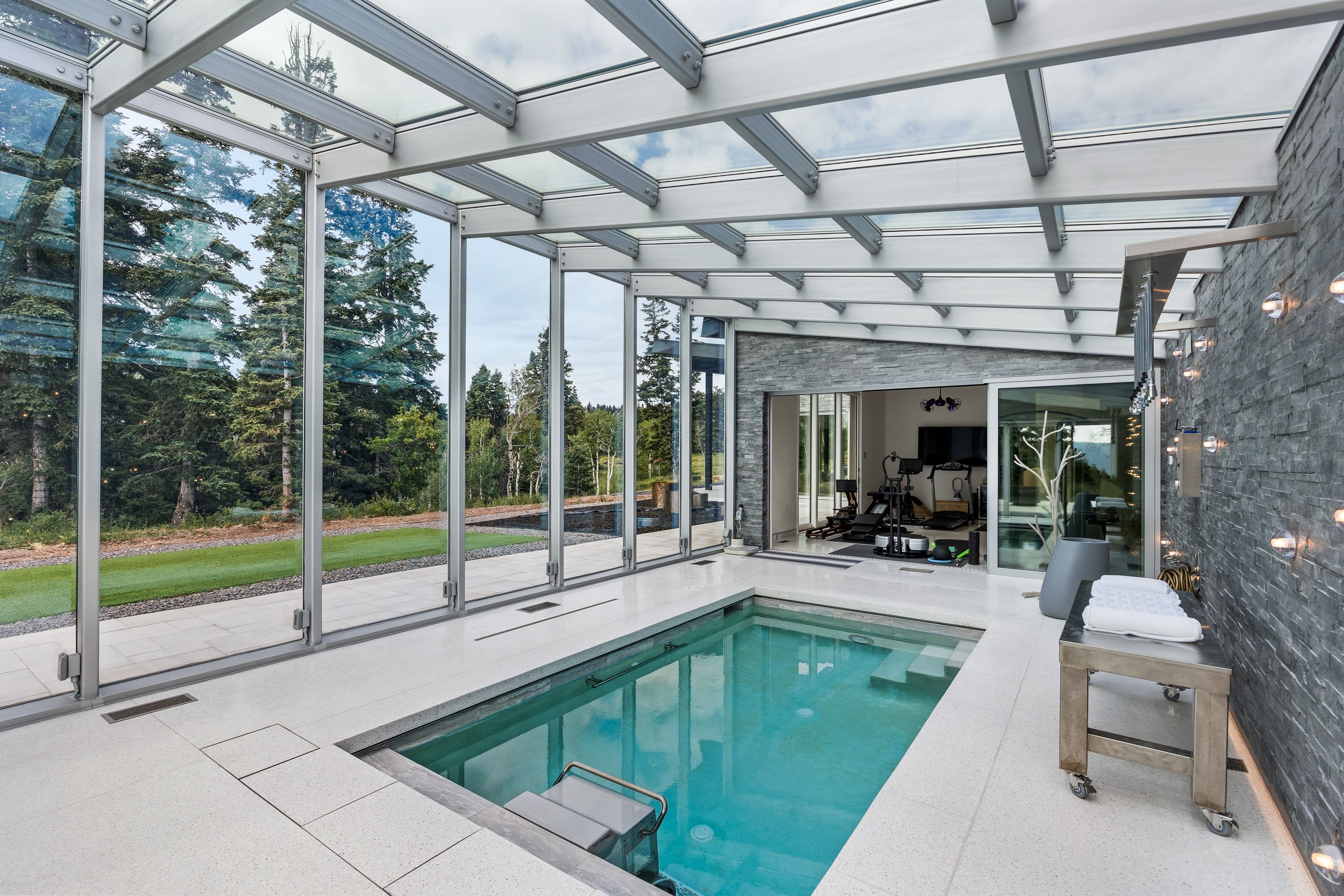 Indoor pool enclosure featuring a glass roof and retractable glass walls