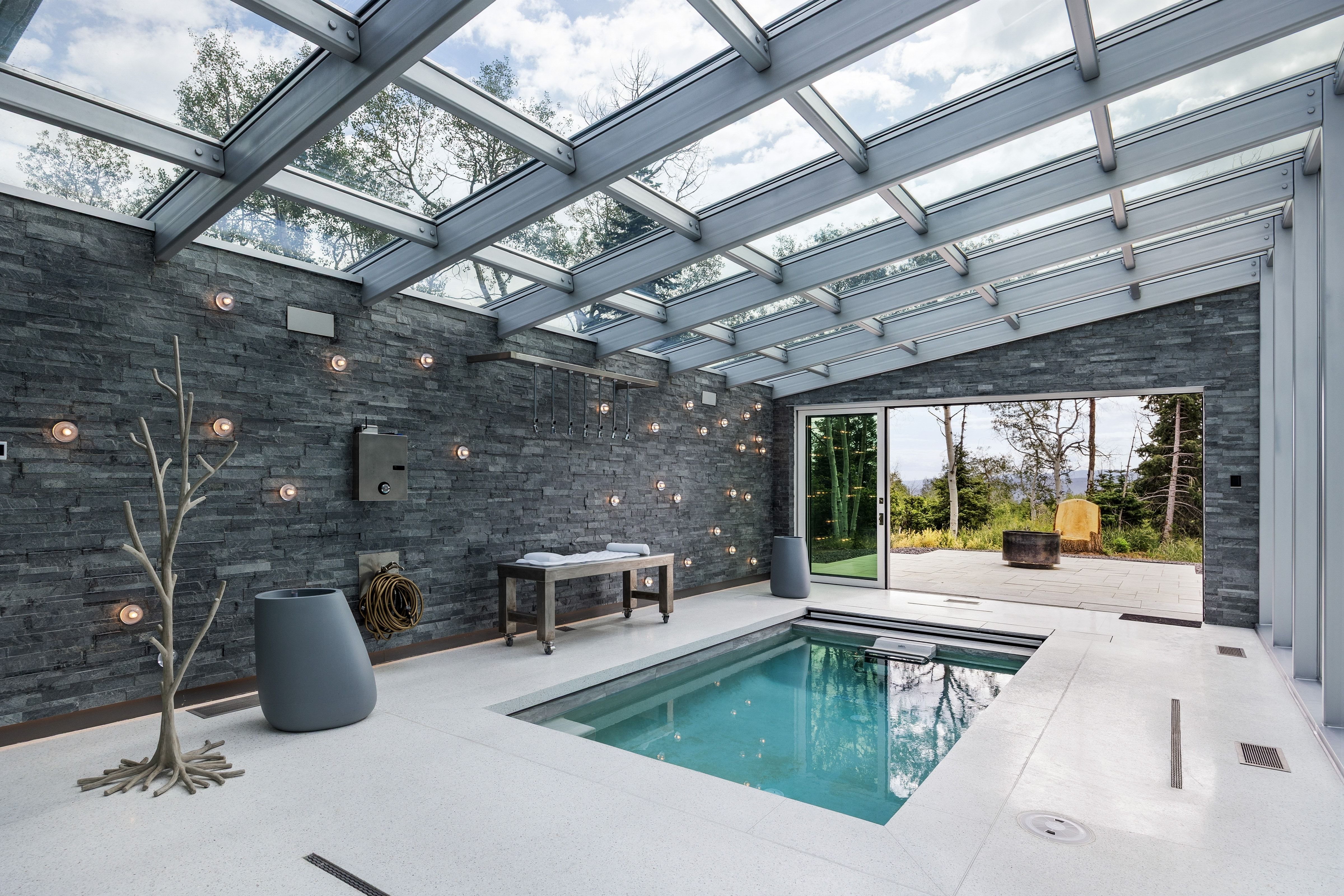 Indoor swimming pool featuring a glass ceiling, stone accent walls, integrated lighting, and direct access to an outdoor patio