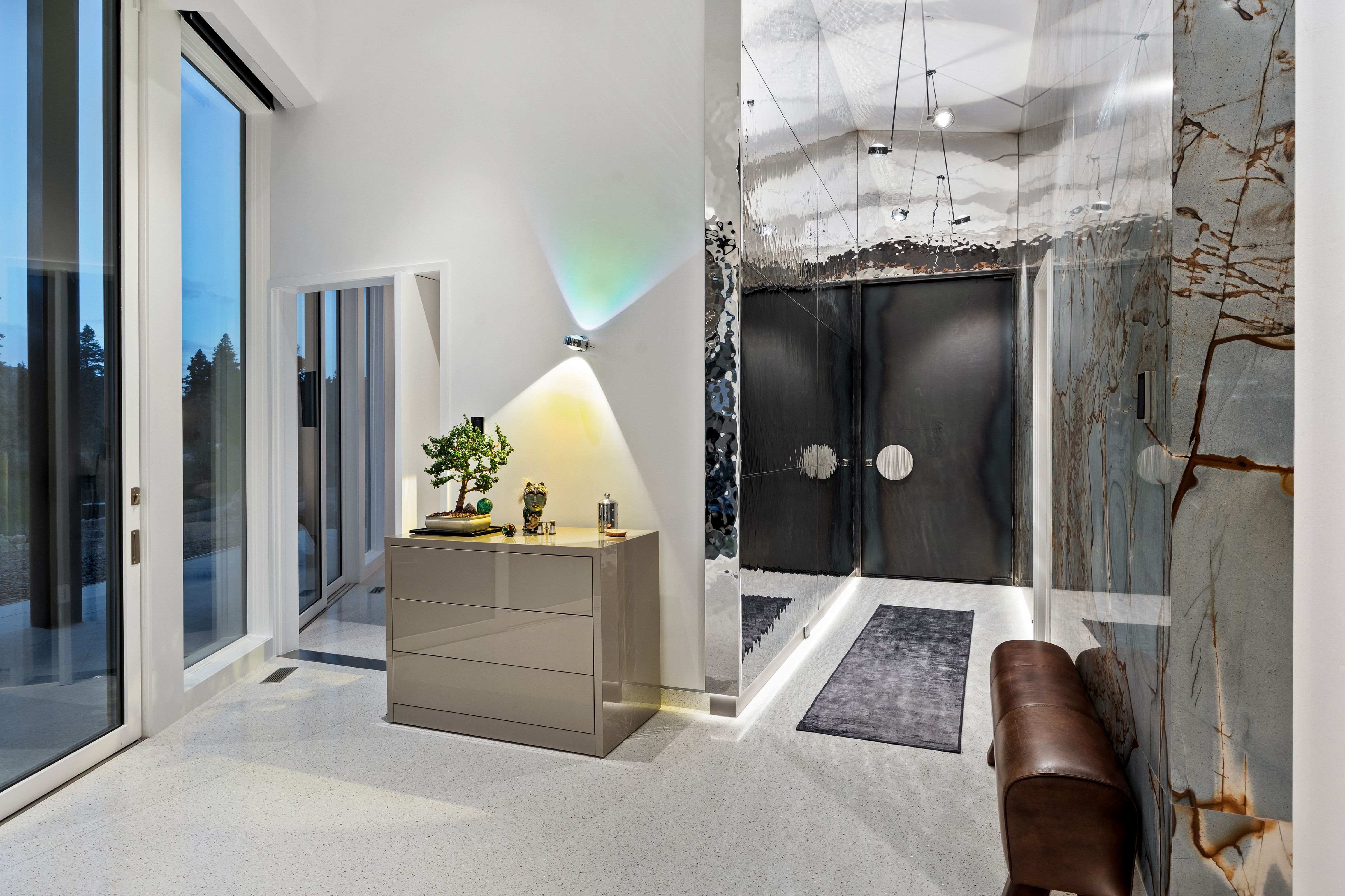 Modern entryway featuring full-height windows, light-toned flooring, a polished stone accent wall, and double entry doors with circular hardware