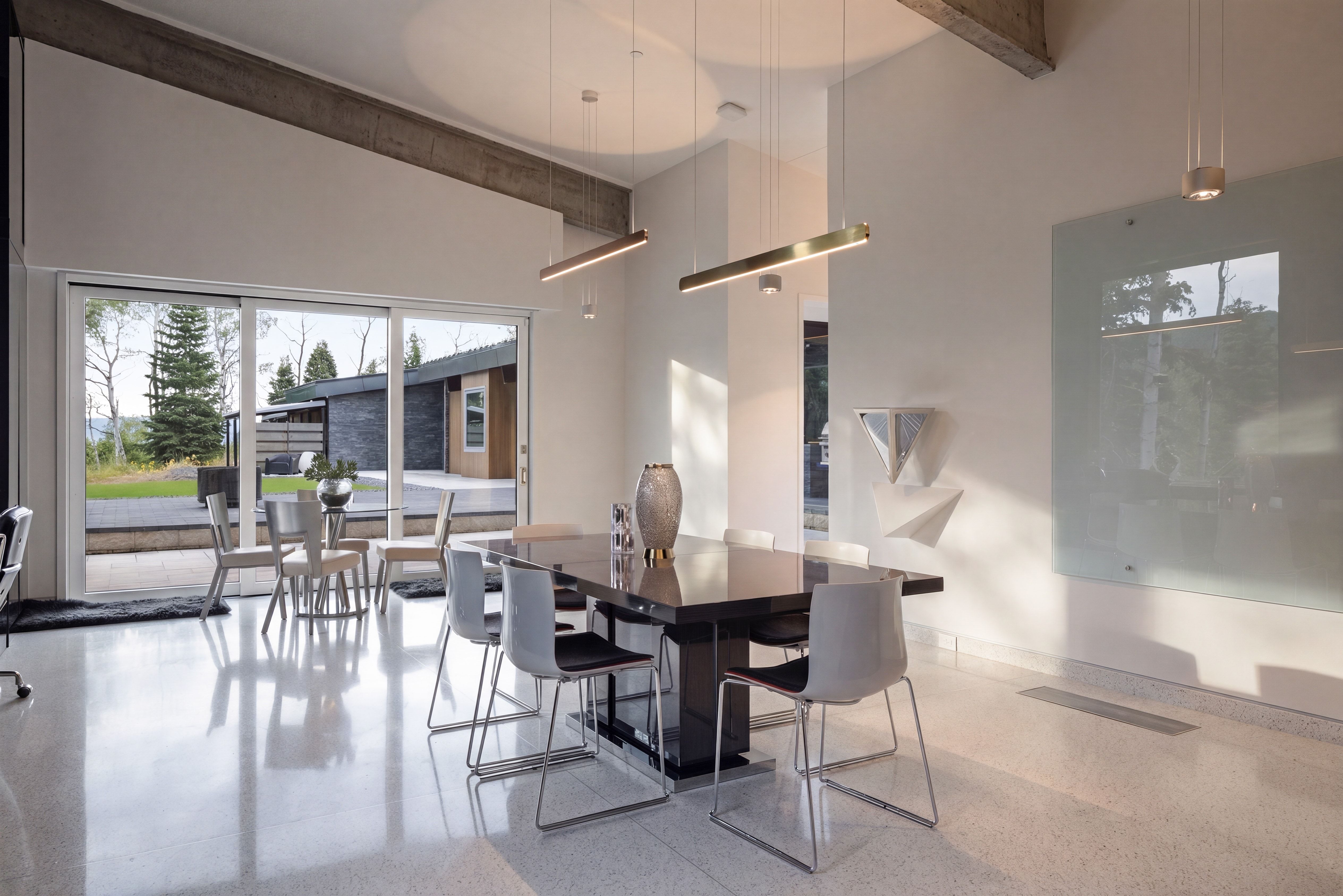 Spacious interior with polished concrete flooring, extensive sliding glass doors, exposed concrete ceiling beams, and contemporary pendant lighting fixtures