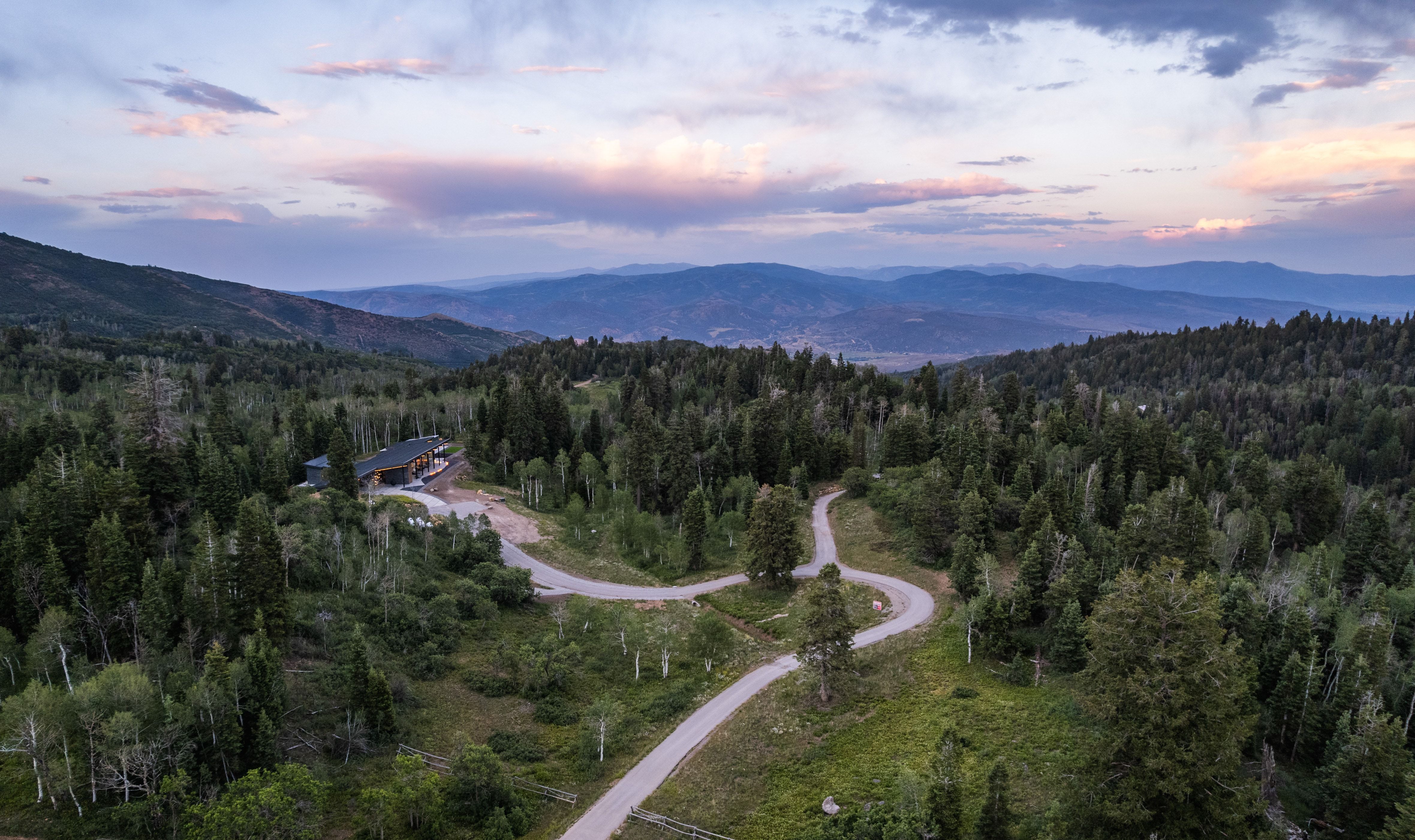 Mountain property featuring a single-family residence, extensive evergreen forests, winding paved driveways, and expansive mountain scenery