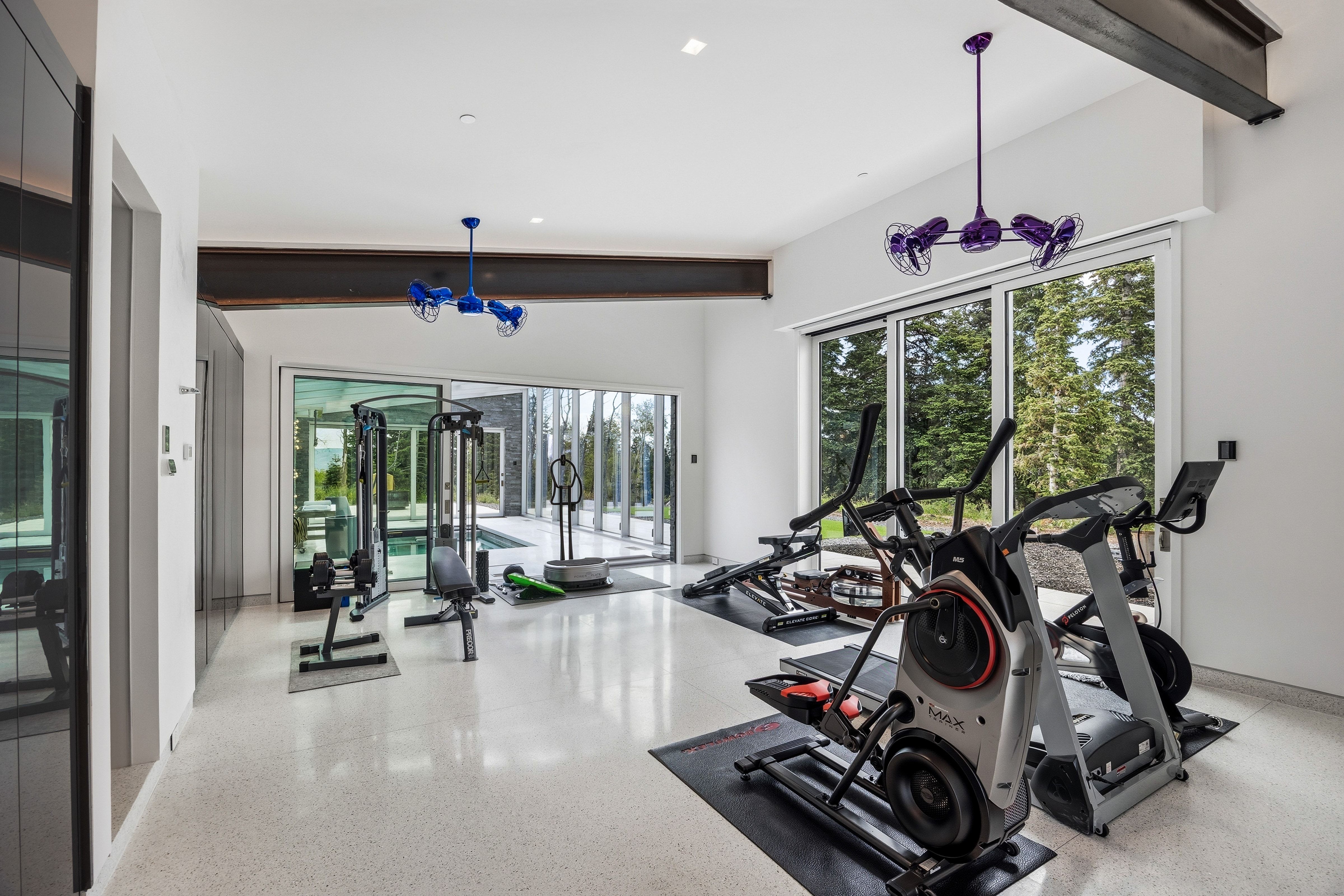 Spacious interior fitness area featuring large format windows, exposed structural beams, high ceilings, and white terrazzo-style flooring