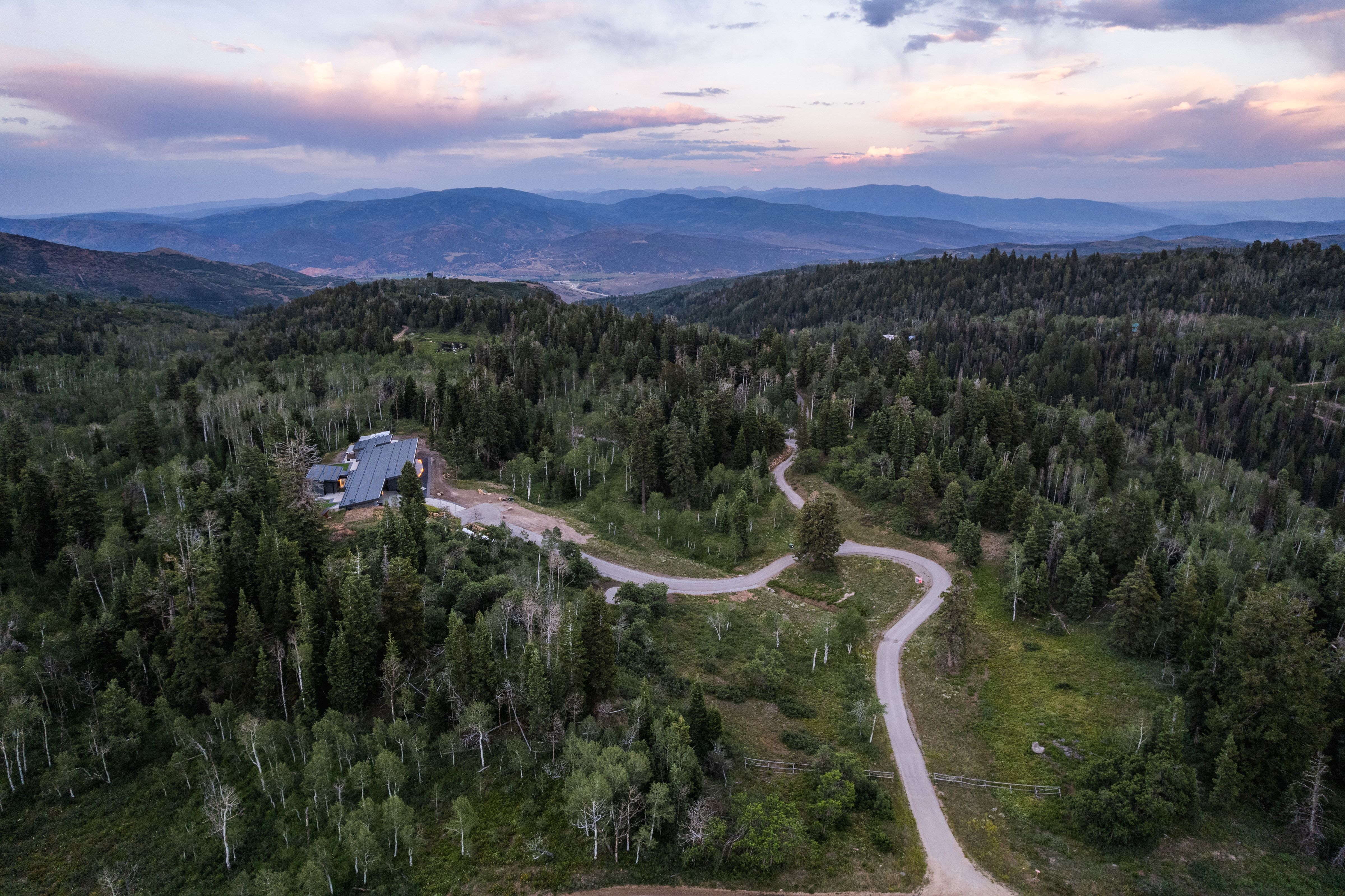 Mountain property with a large, dark-toned roof, surrounded by extensive evergreen and deciduous tree coverage