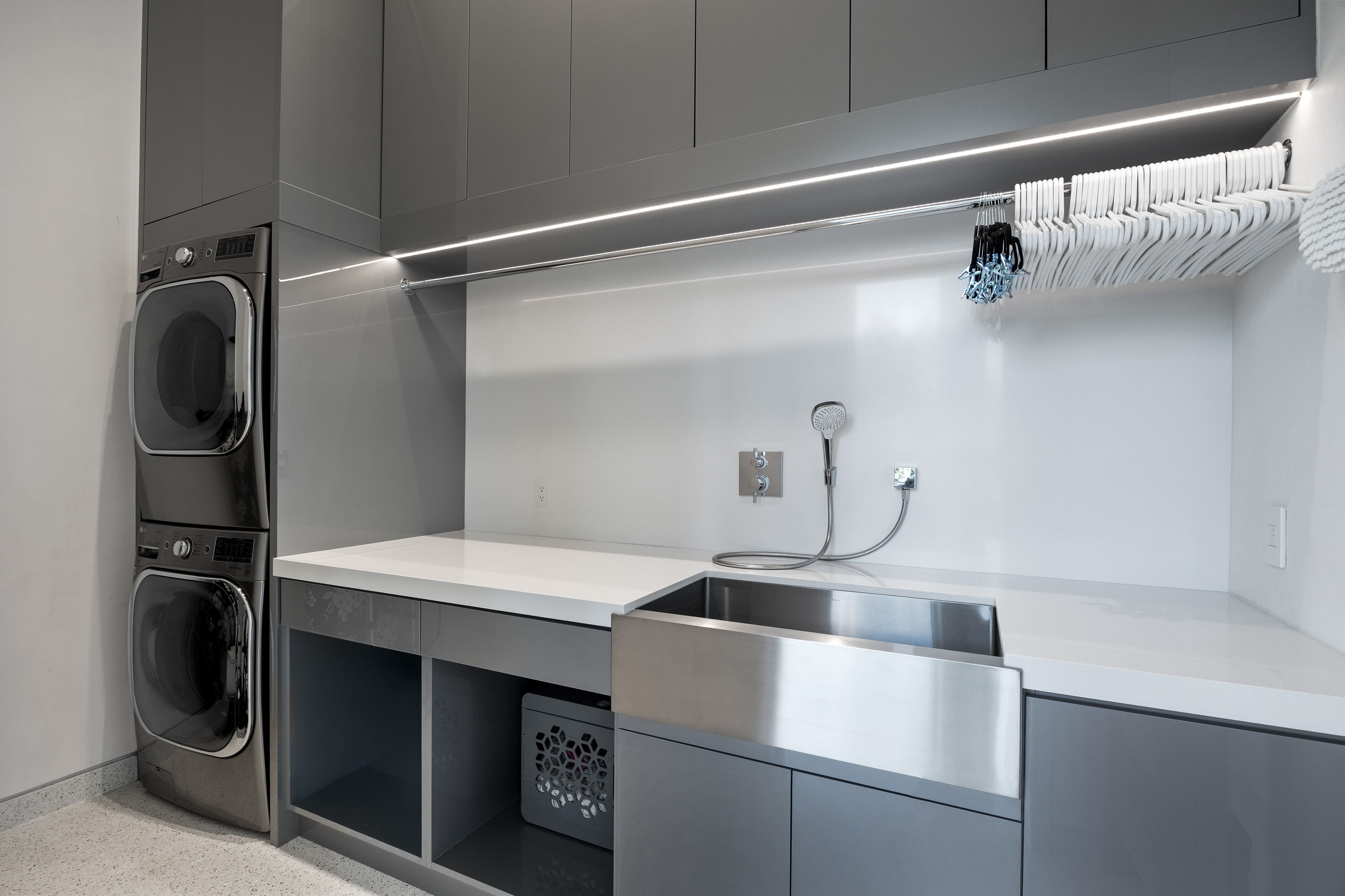 Modern laundry area featuring stacked appliances, extensive cabinetry, and a large farmhouse-style sink with a pull-down sprayer
