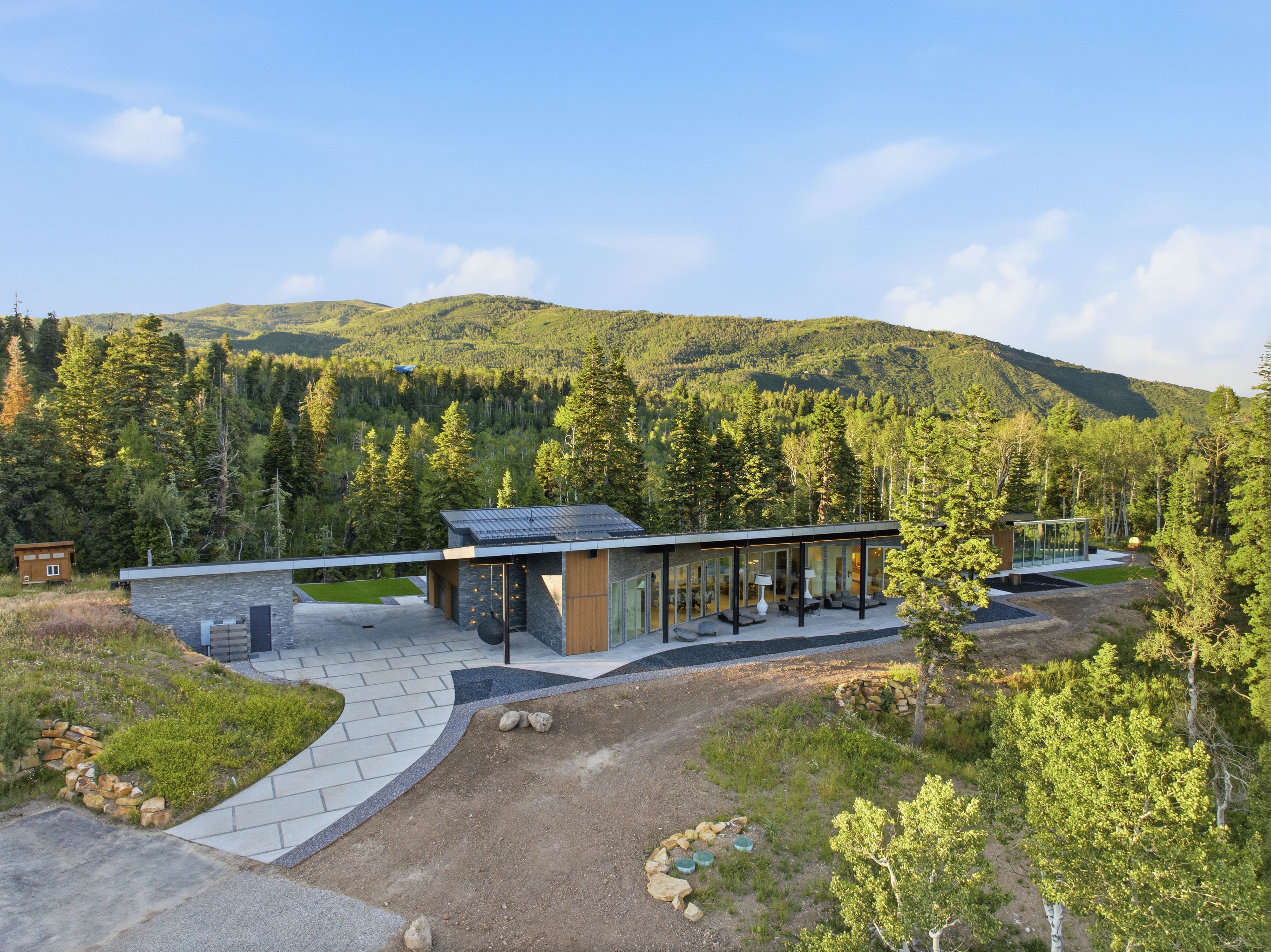 Contemporary architectural residence featuring an expansive patio, extensive window walls, and mature surrounding trees