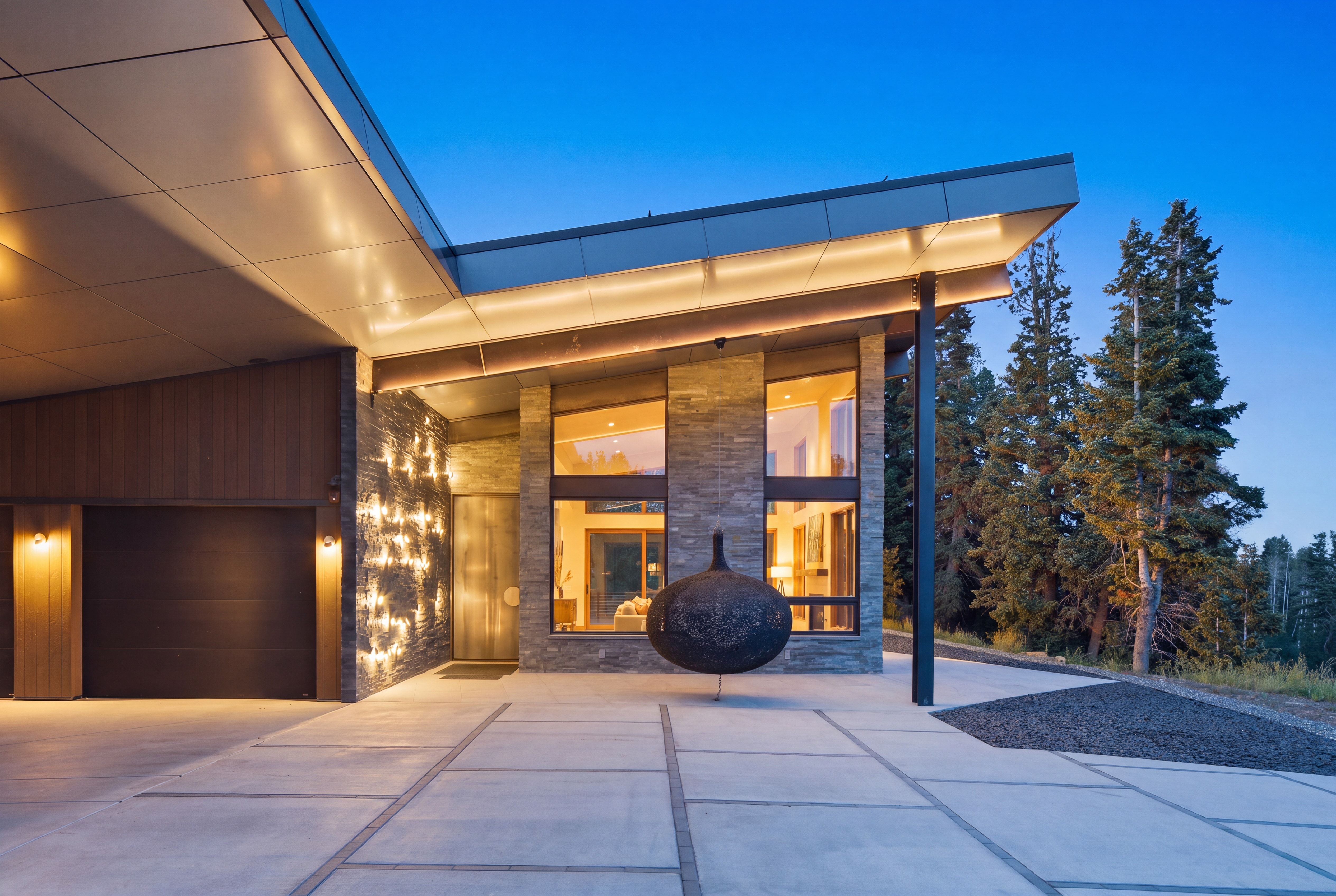 Modern architectural exterior featuring a stone facade, wood paneling, a dark garage door, expansive windows, and a concrete paver driveway