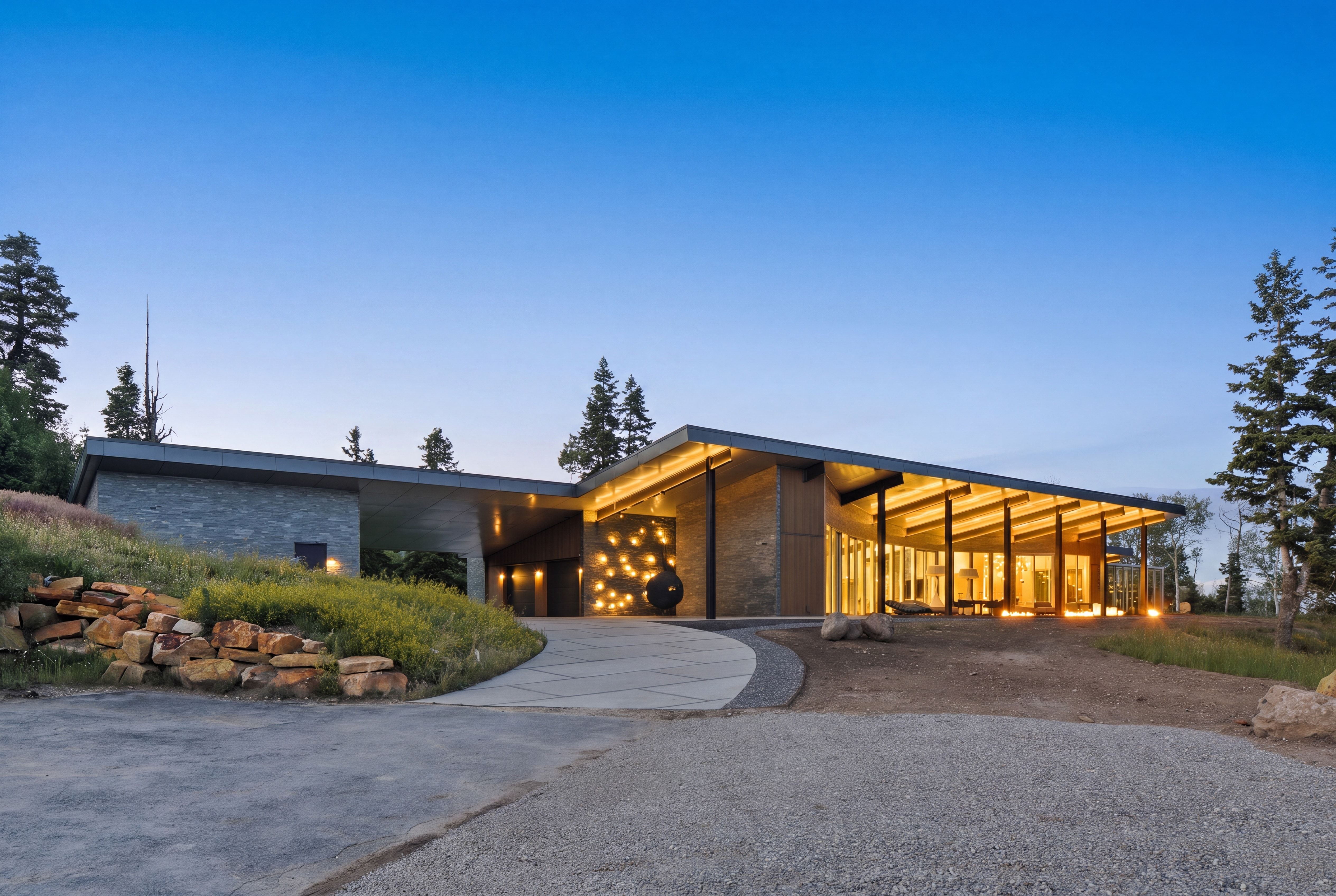 Contemporary residence featuring an expansive overhang, large glass facade, natural stone accents, and a curved concrete driveway