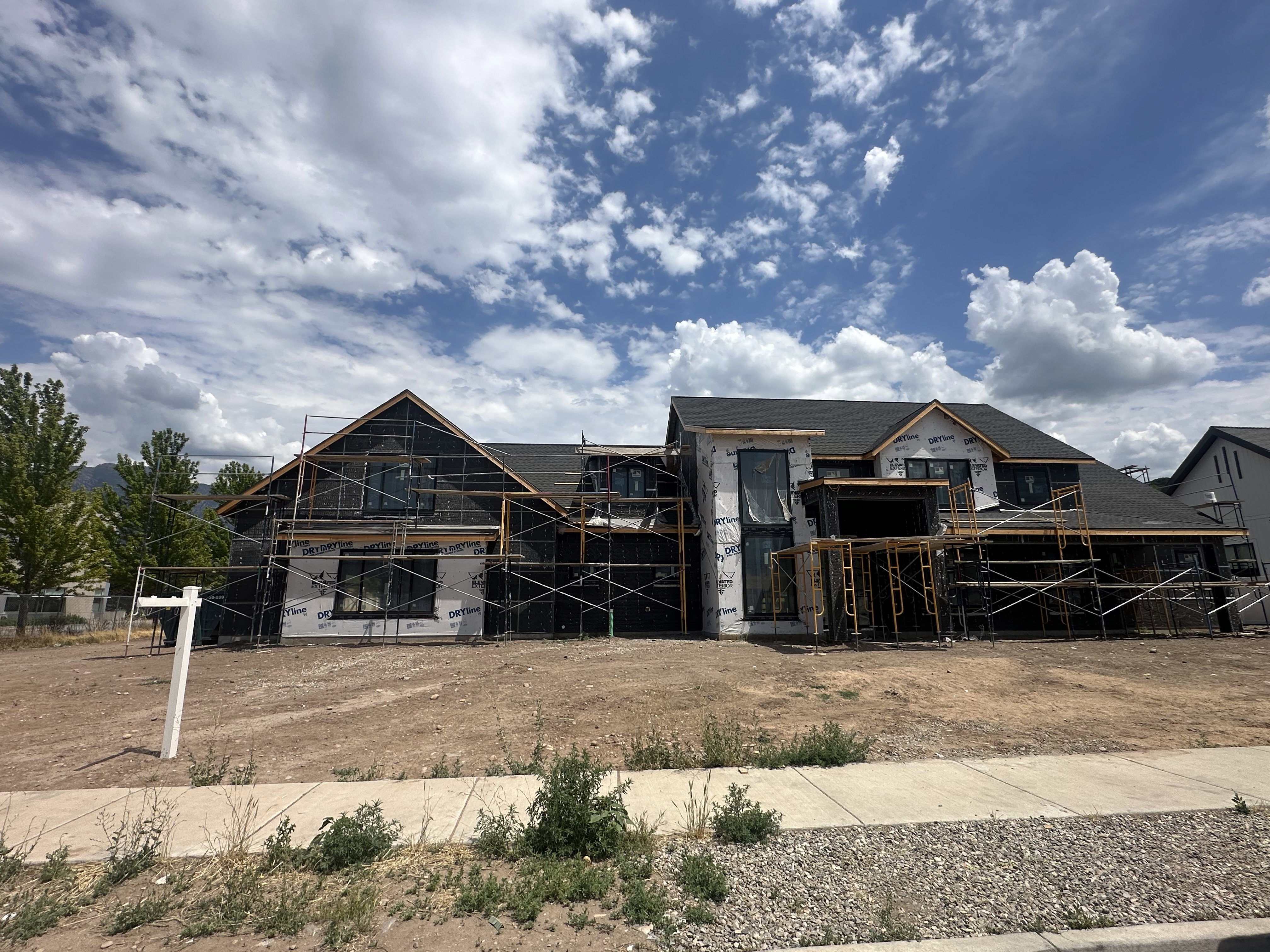 New construction residential structure featuring a dark shingle roof and a combination of wall sheathing and house wrap