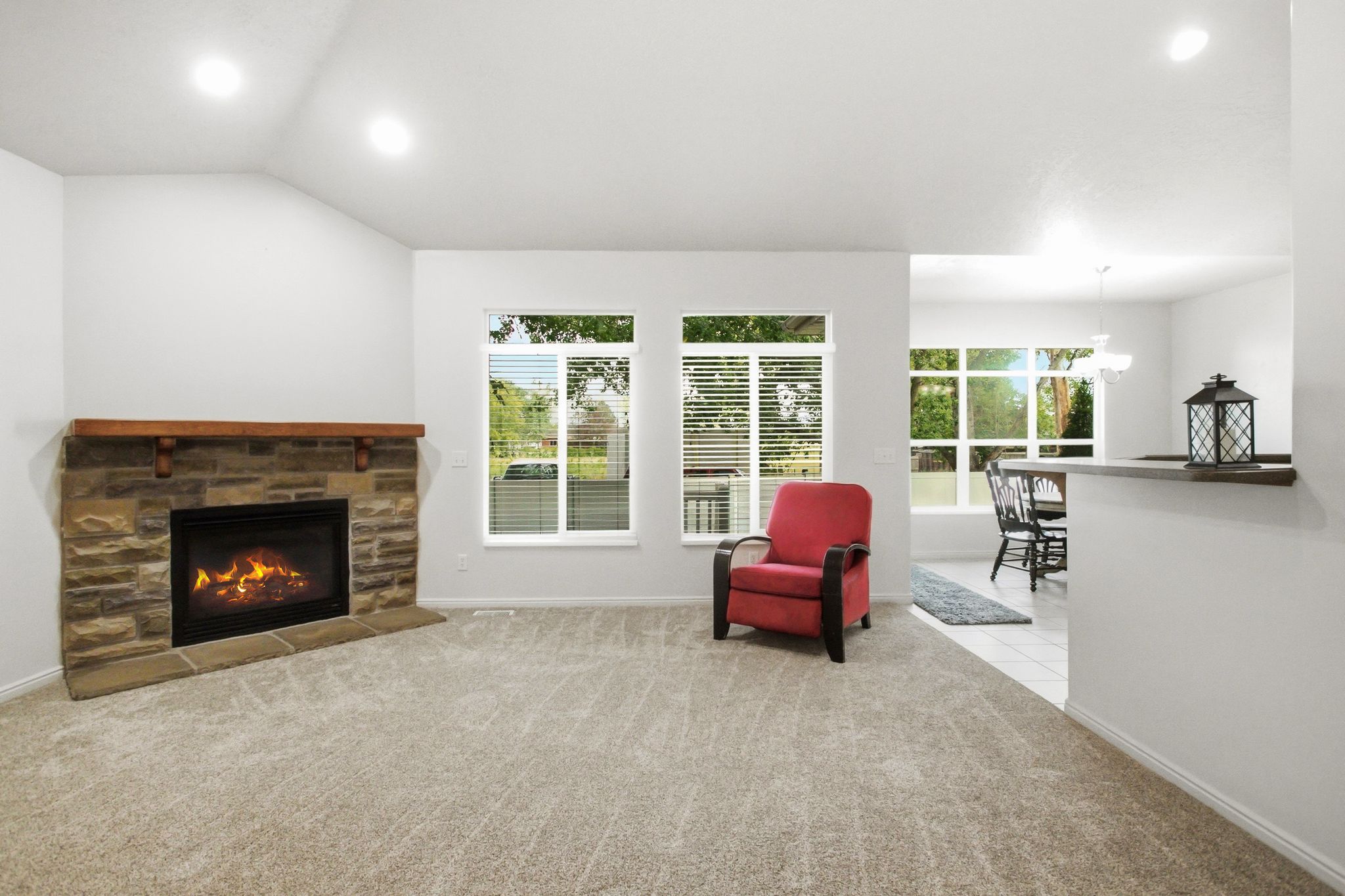 Living area featuring a stone-clad fireplace with a wood mantel, vaulted ceilings, and recessed lighting