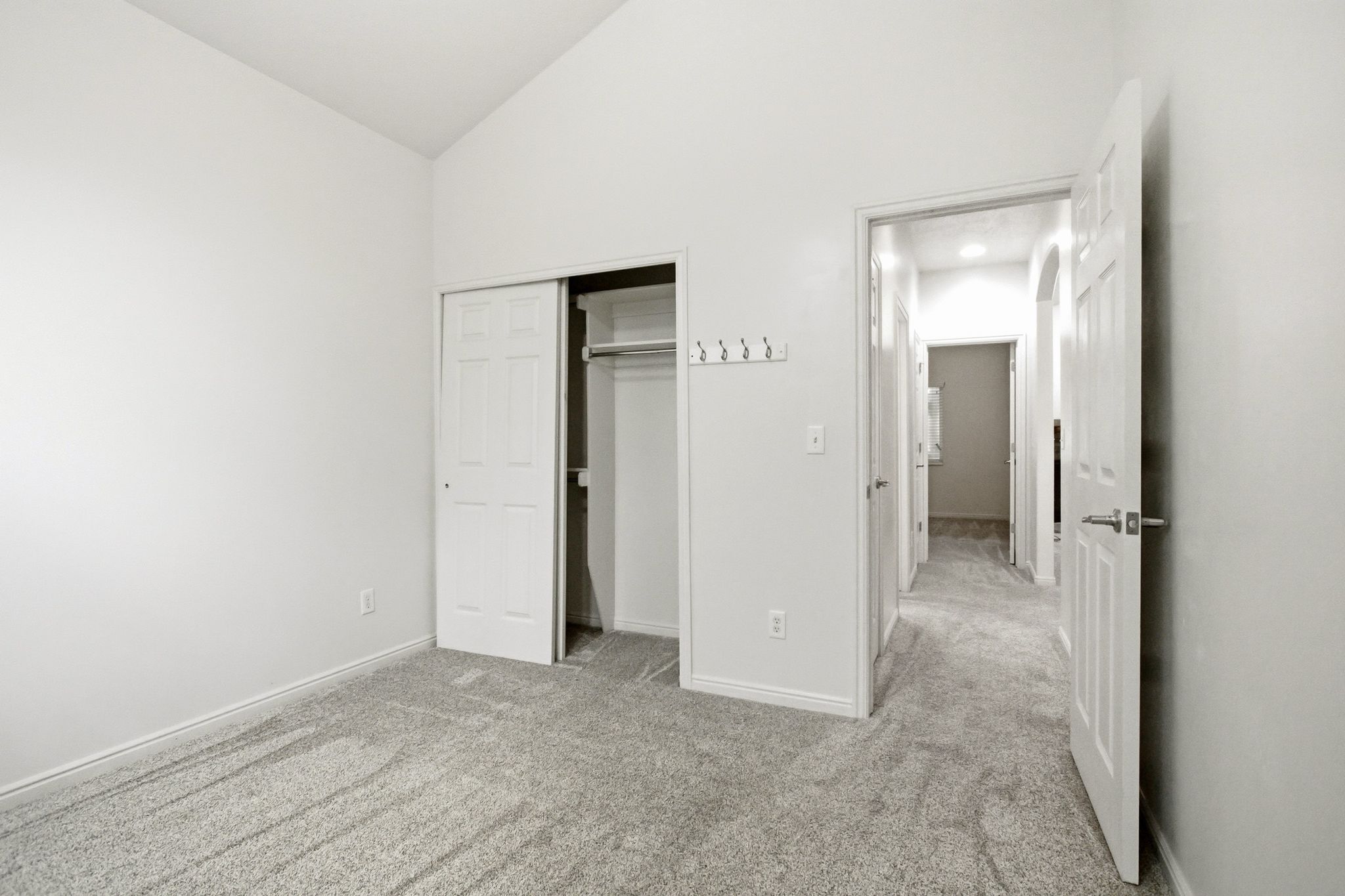 Vaulted ceiling room featuring light gray carpet, white baseboards, and a bi-fold closet with a visible closet rod