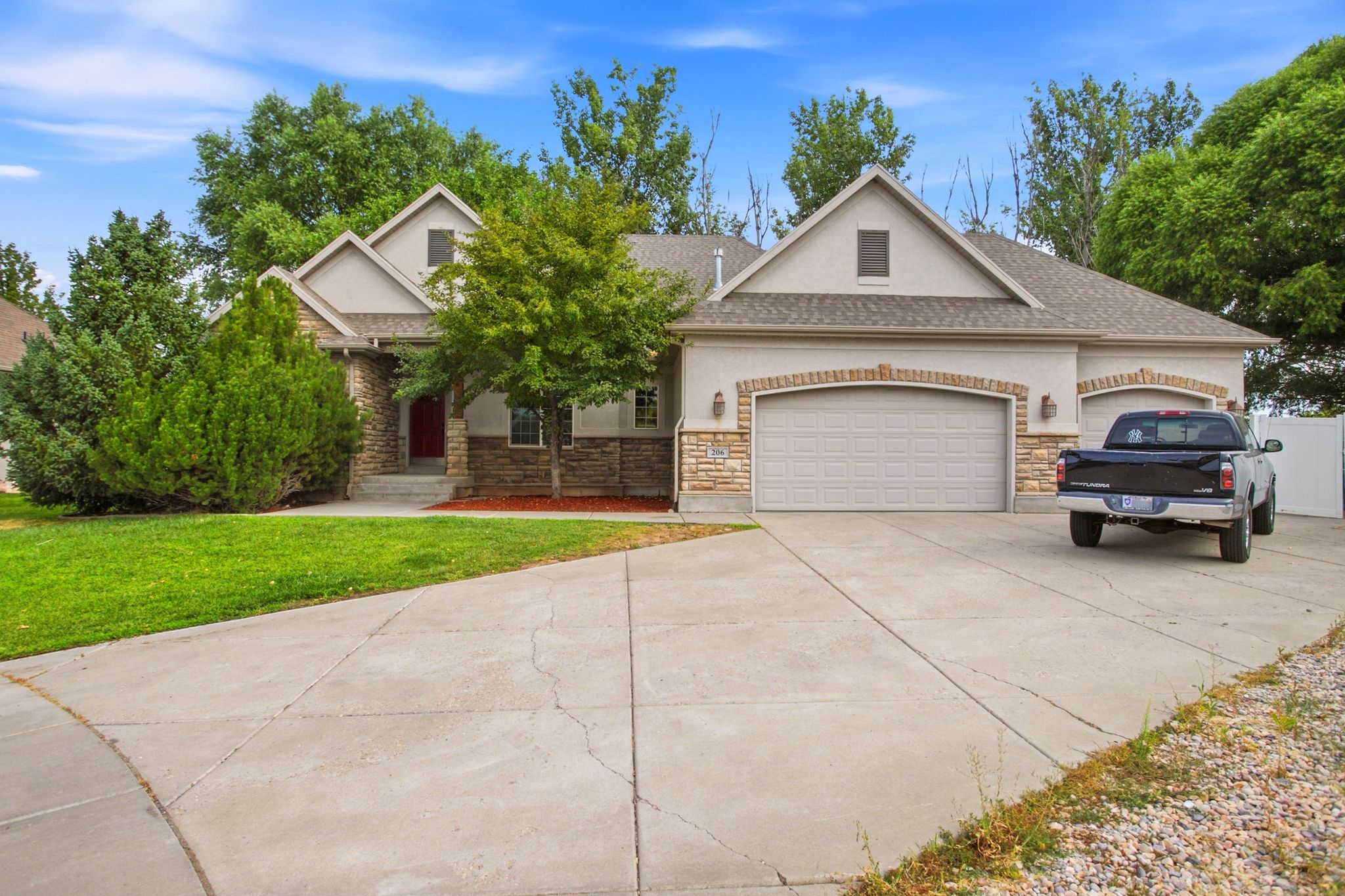 Stucco and stone facade home featuring a two-car garage, arched garage door detailing, a large concrete driveway, and mature landscaping