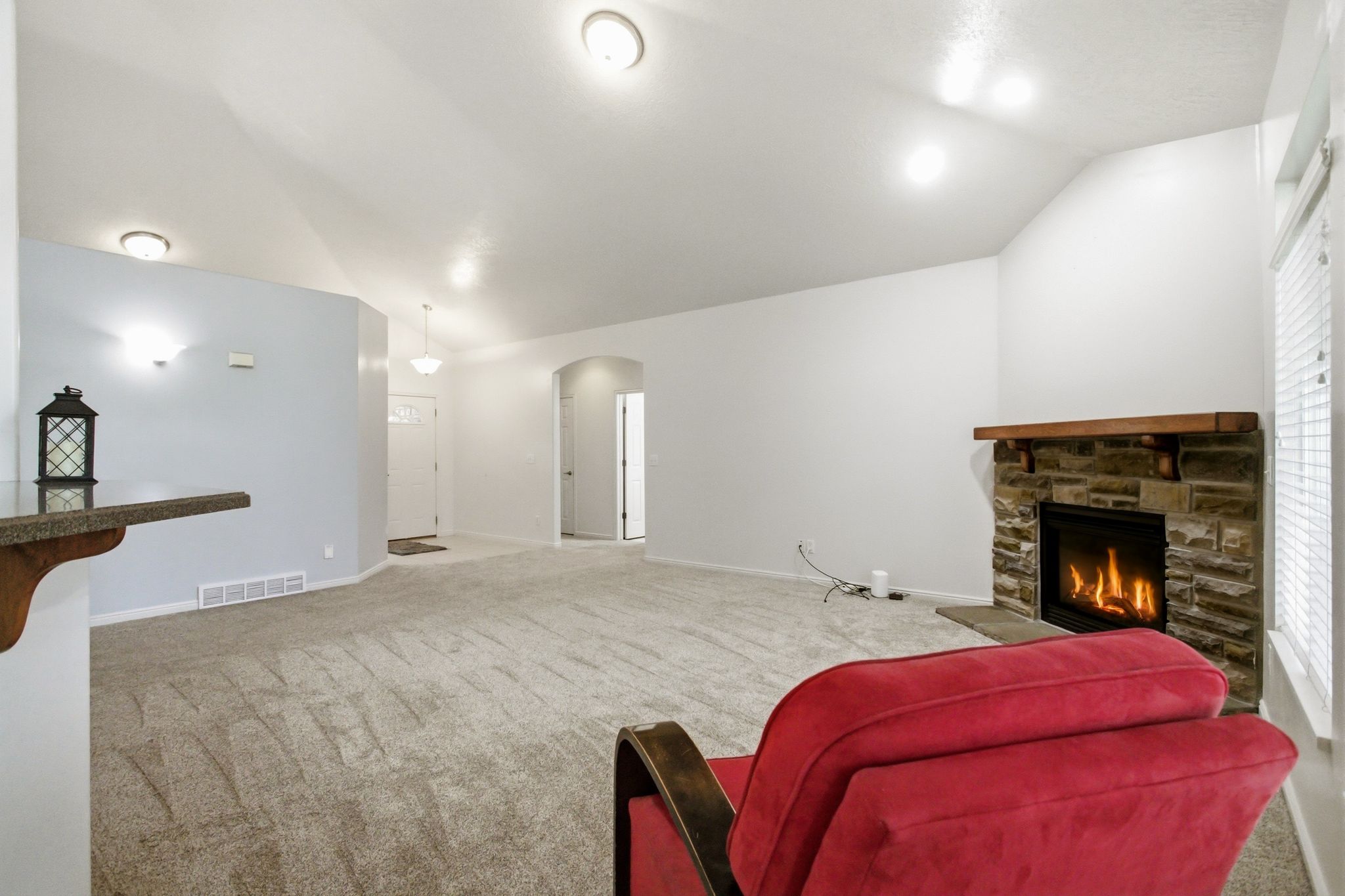 Living area featuring a stone fireplace with a wood-finish mantle, vaulted ceilings, recessed lighting, and soft carpeting