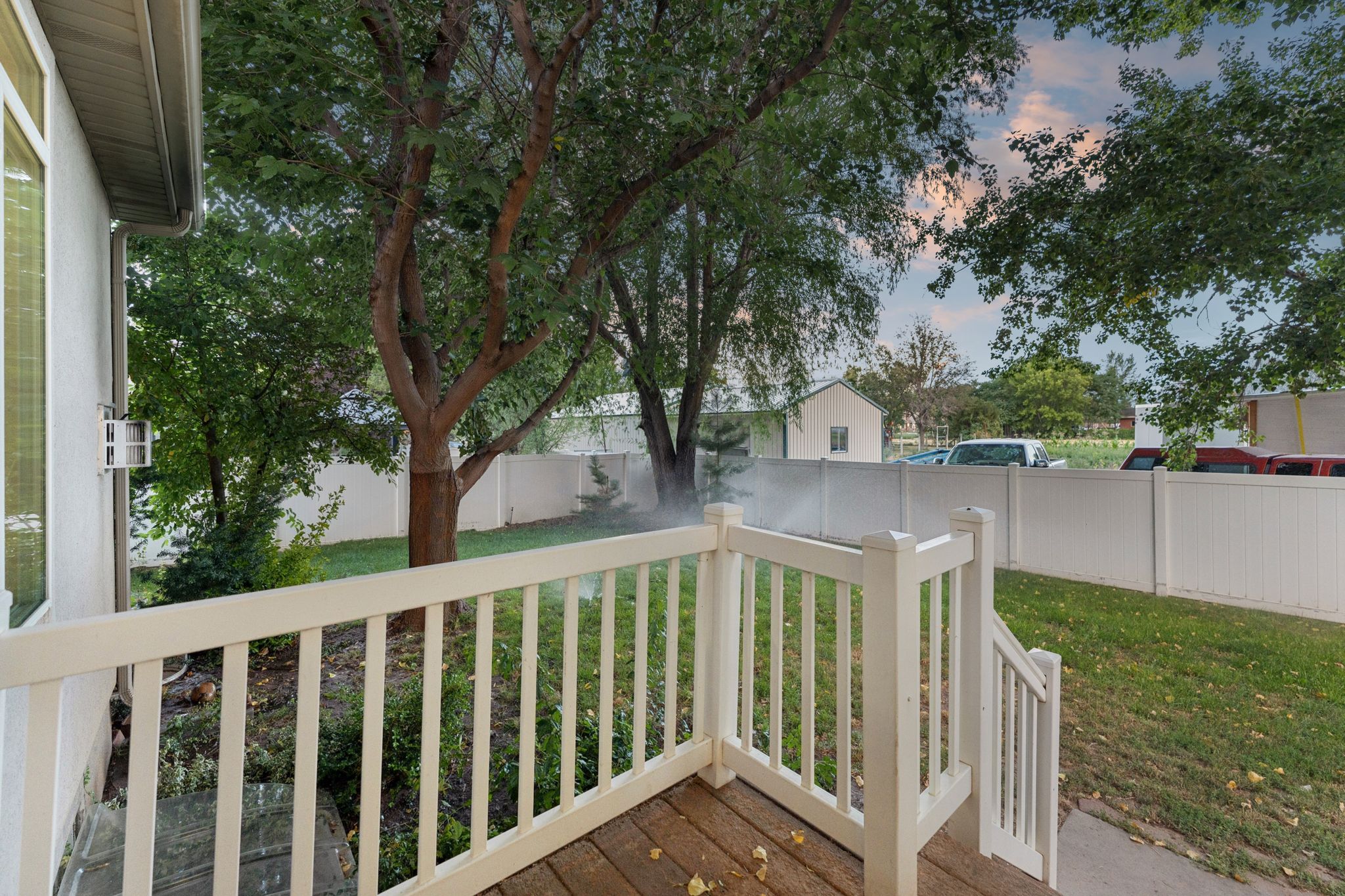 Wood-finish deck with white railings overlooks a green lawn, mature trees, and a white privacy fence