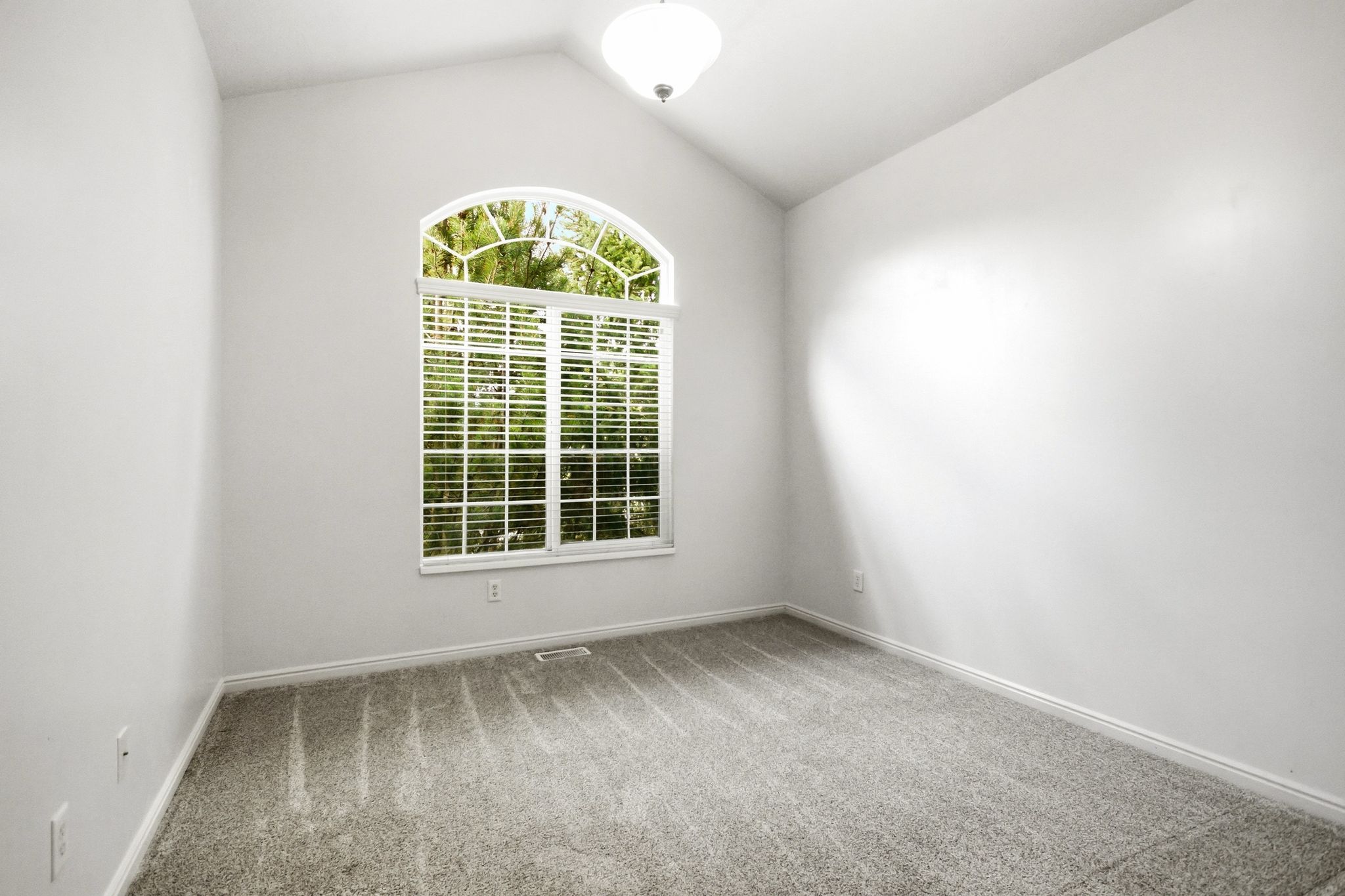 Room featuring a vaulted ceiling, arched top window with white blinds, neutral carpeting, and a flush-mount ceiling light fixture