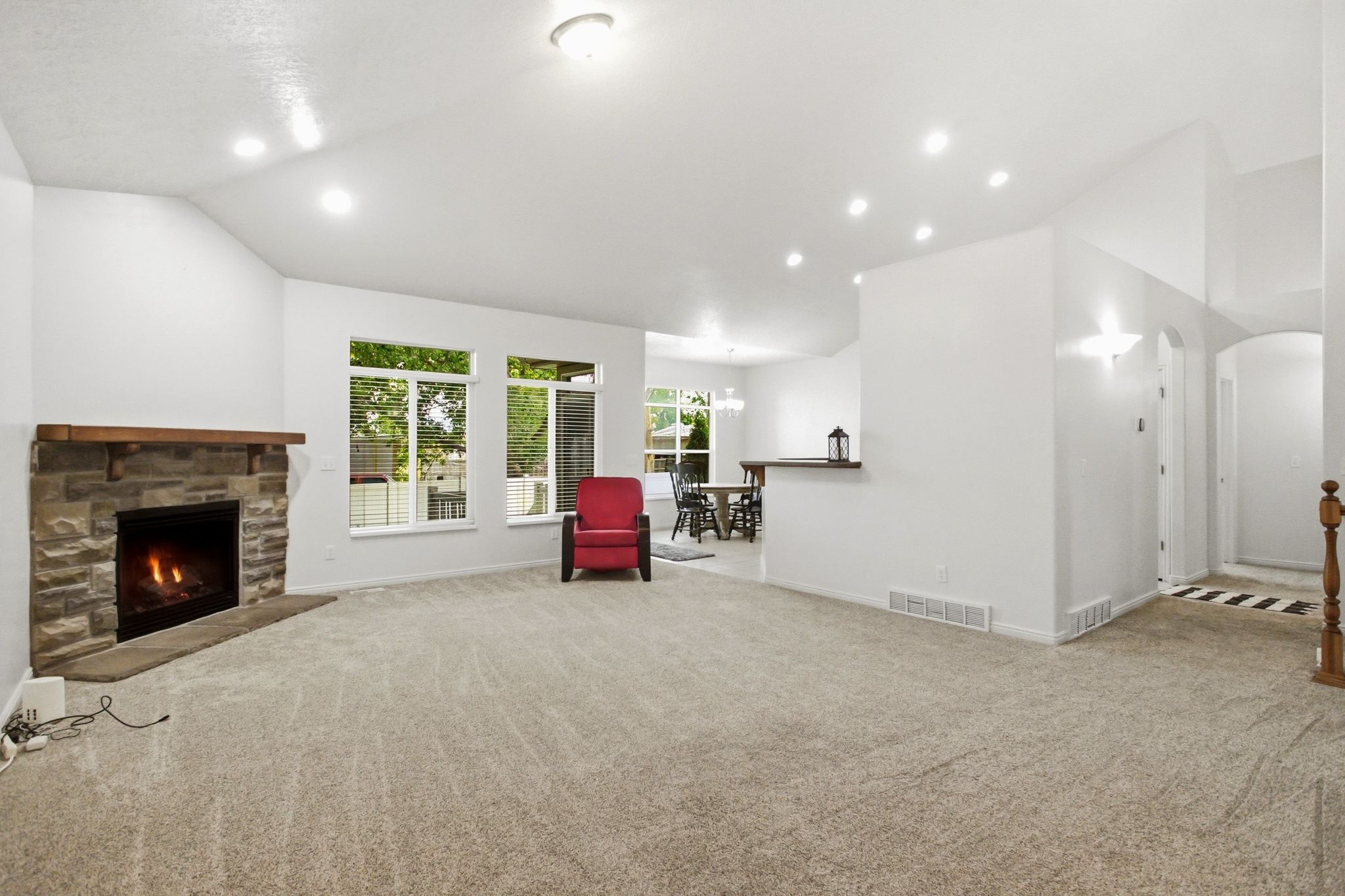 Spacious living area featuring a stone-clad fireplace with a wood mantle, vaulted ceilings with recessed lighting, and multiple windows