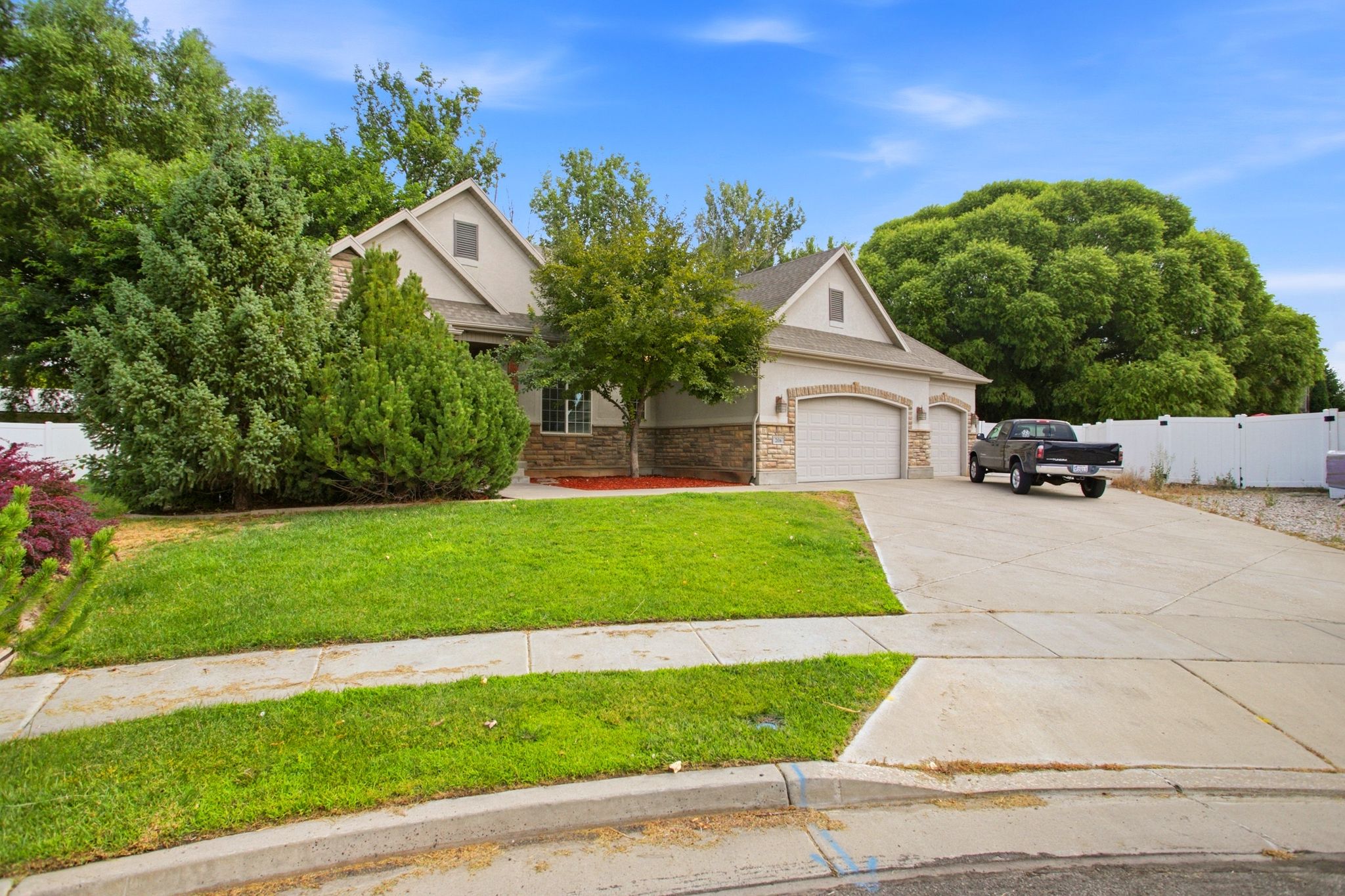 Contemporary stucco and stone-veneer exterior with a multi-car driveway, attached garage, and manicured front lawn