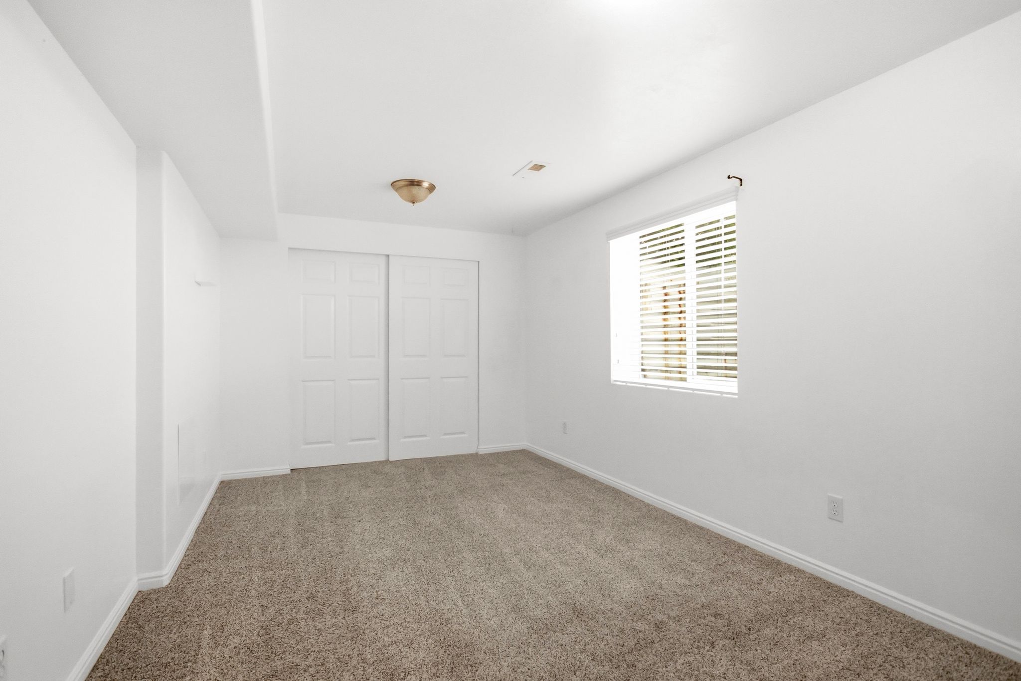 Carpeted room featuring a window with blinds, white walls, and a ceiling-mounted light fixture