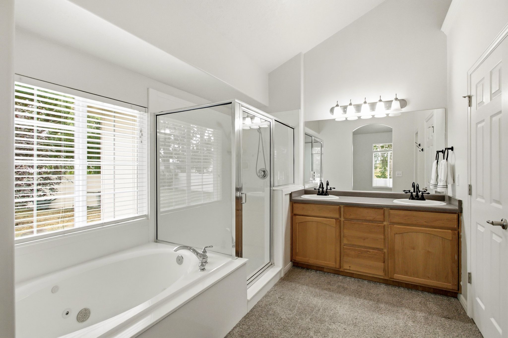 Bathroom featuring a jetted soaking tub, glass-enclosed shower, dual vanity with wood cabinetry, and vaulted ceilings