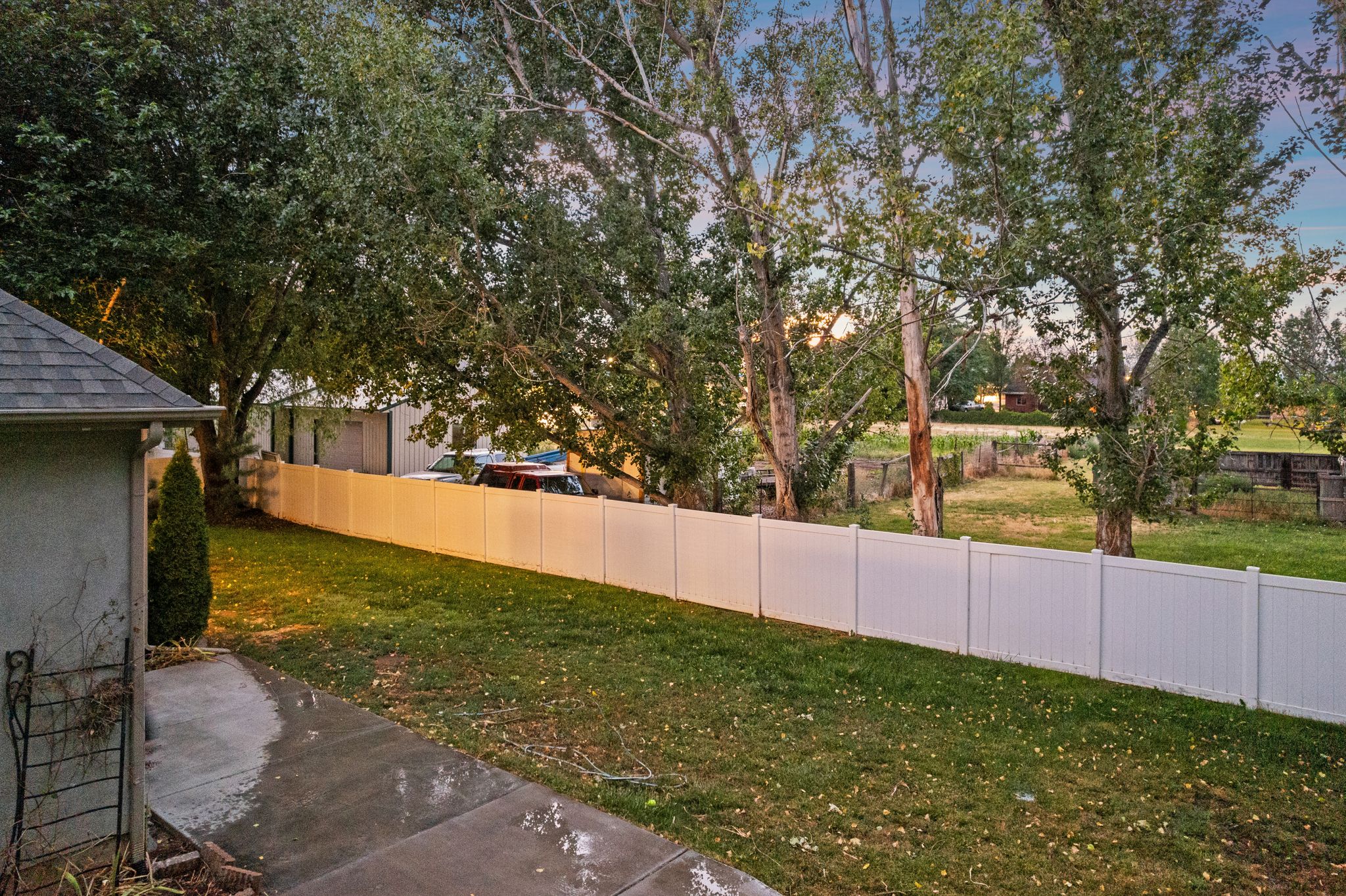 Expansive yard with a manicured lawn, mature trees, and a durable white privacy fence