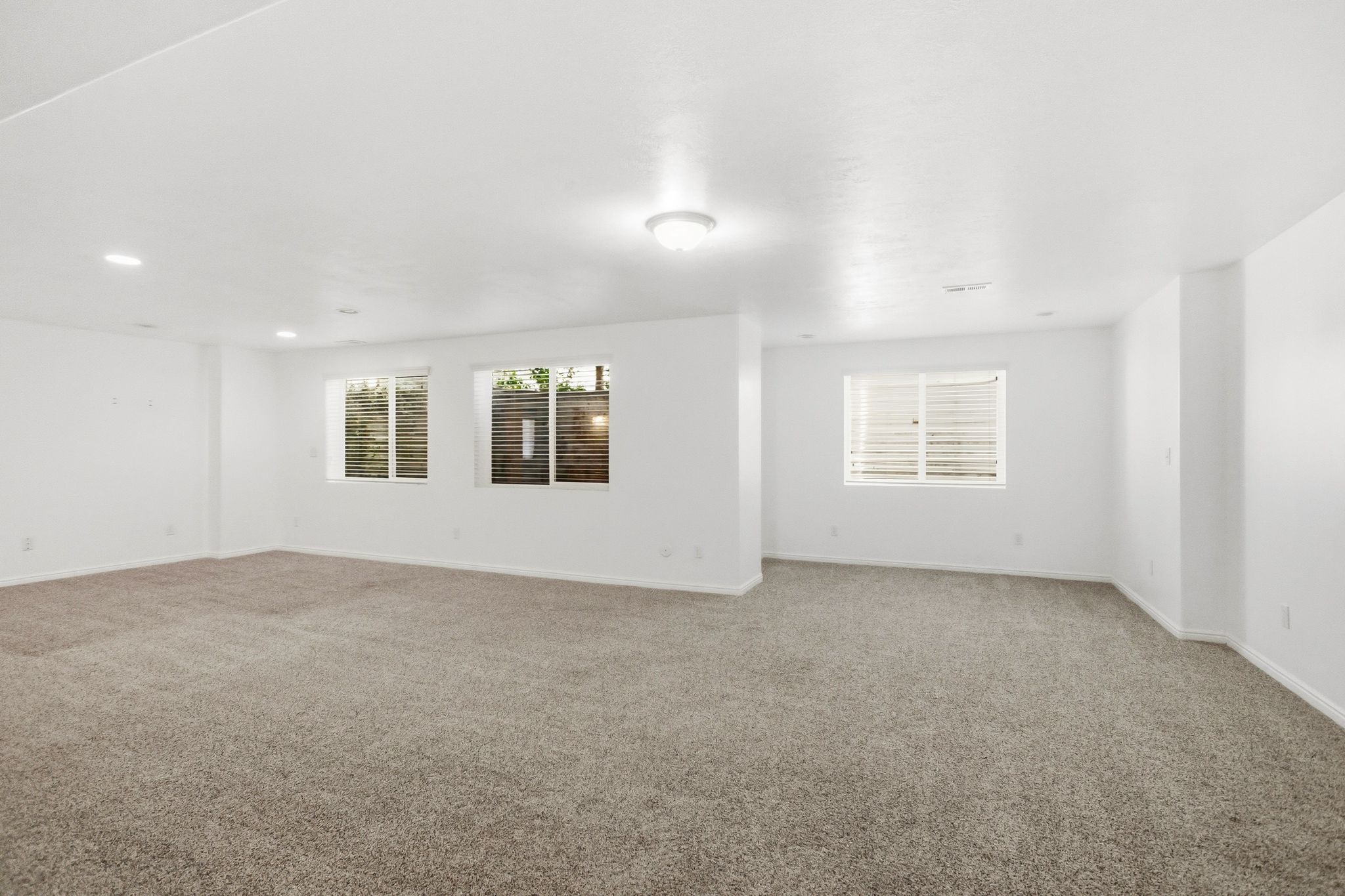 Spacious room featuring neutral carpeting, recessed lighting, white walls, and multiple windows providing natural light
