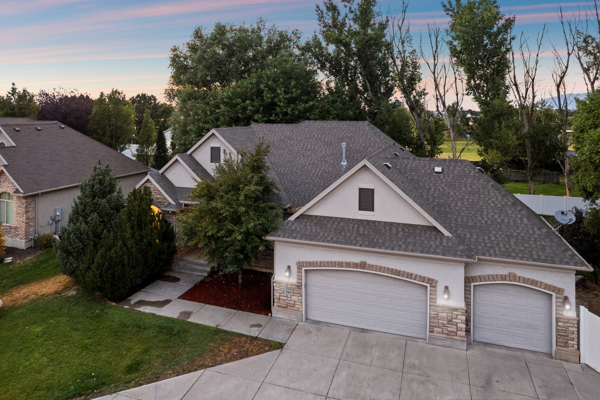 Exterior showcasing a multi-gabled roofline with asphalt shingles, a two-car garage with arched brick detailing, a concrete driveway, and mature landscaping