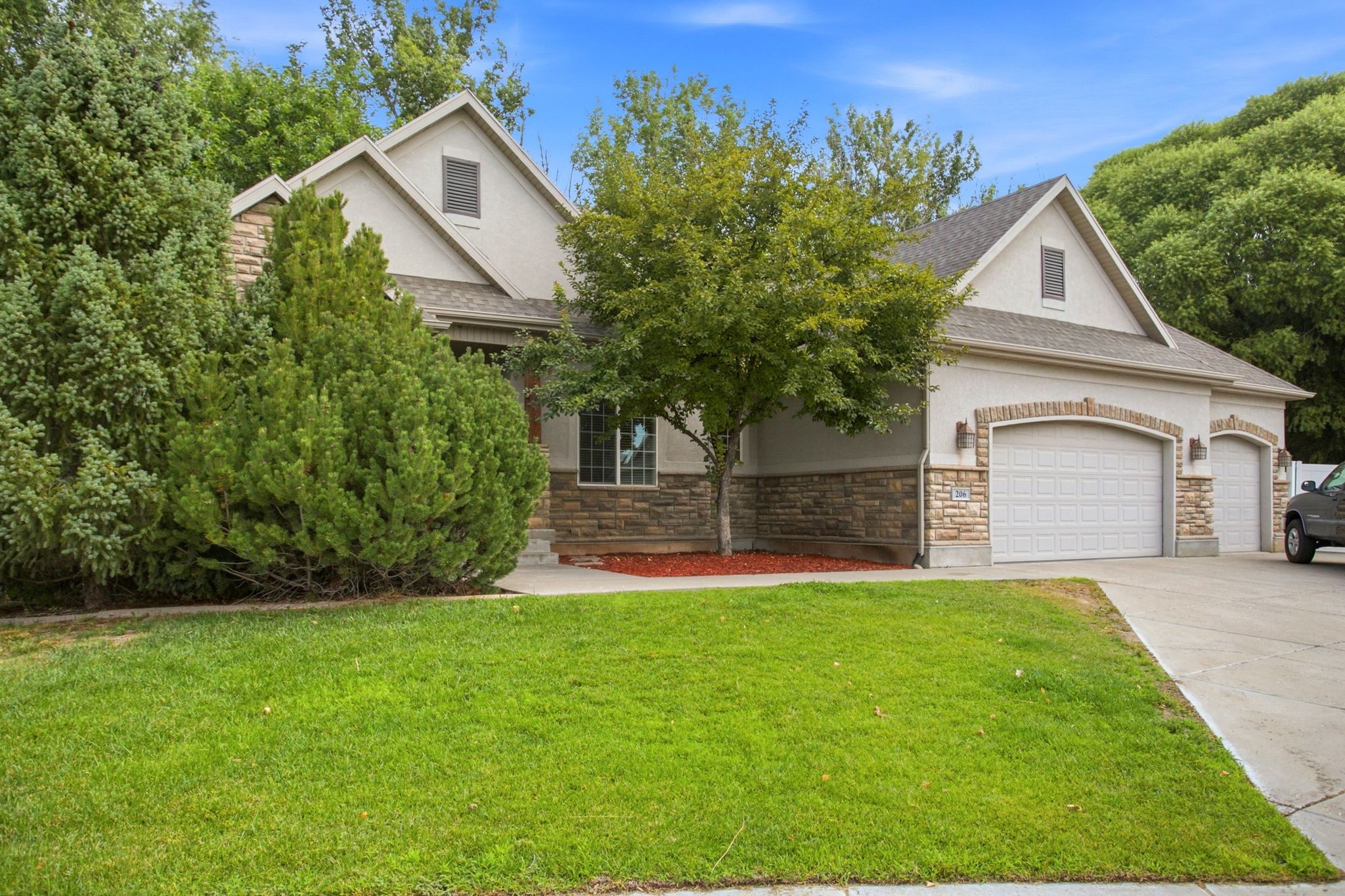 Stucco exterior featuring stone veneer accents and a multi-car garage with arched brick detailing