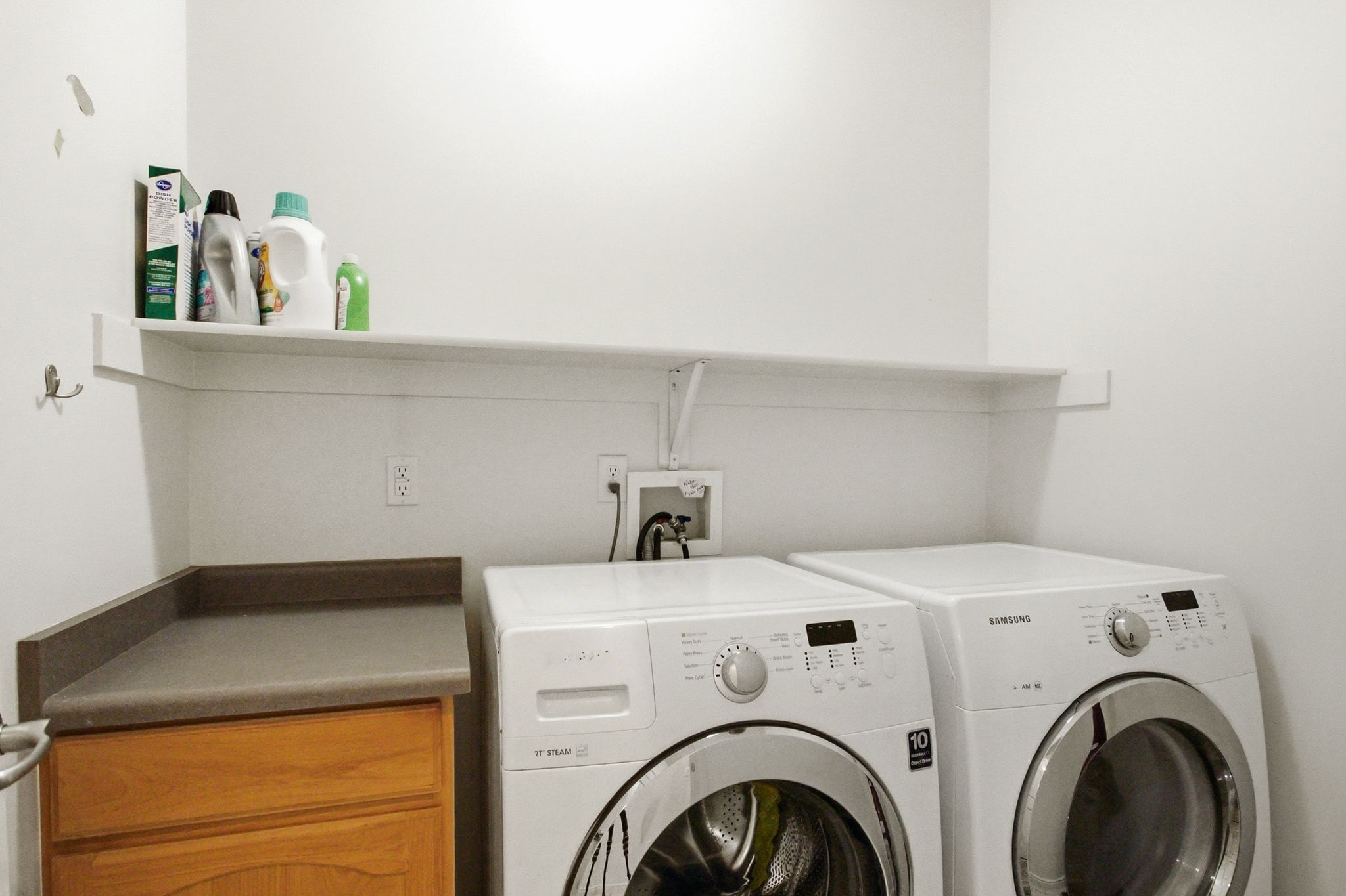 Dedicated laundry area featuring a built-in counter with wood-finish cabinetry, a wall-mounted white shelf, and multiple electrical outlets
