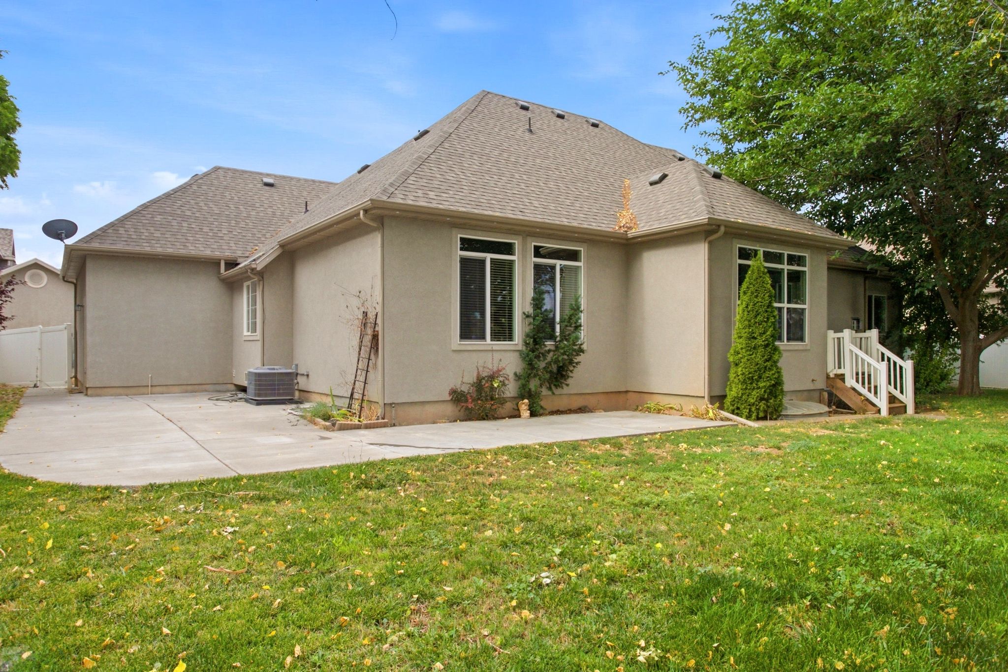 Rear exterior featuring a concrete patio, stucco siding, multiple windows, a white-railed wooden staircase, and a shingled roof