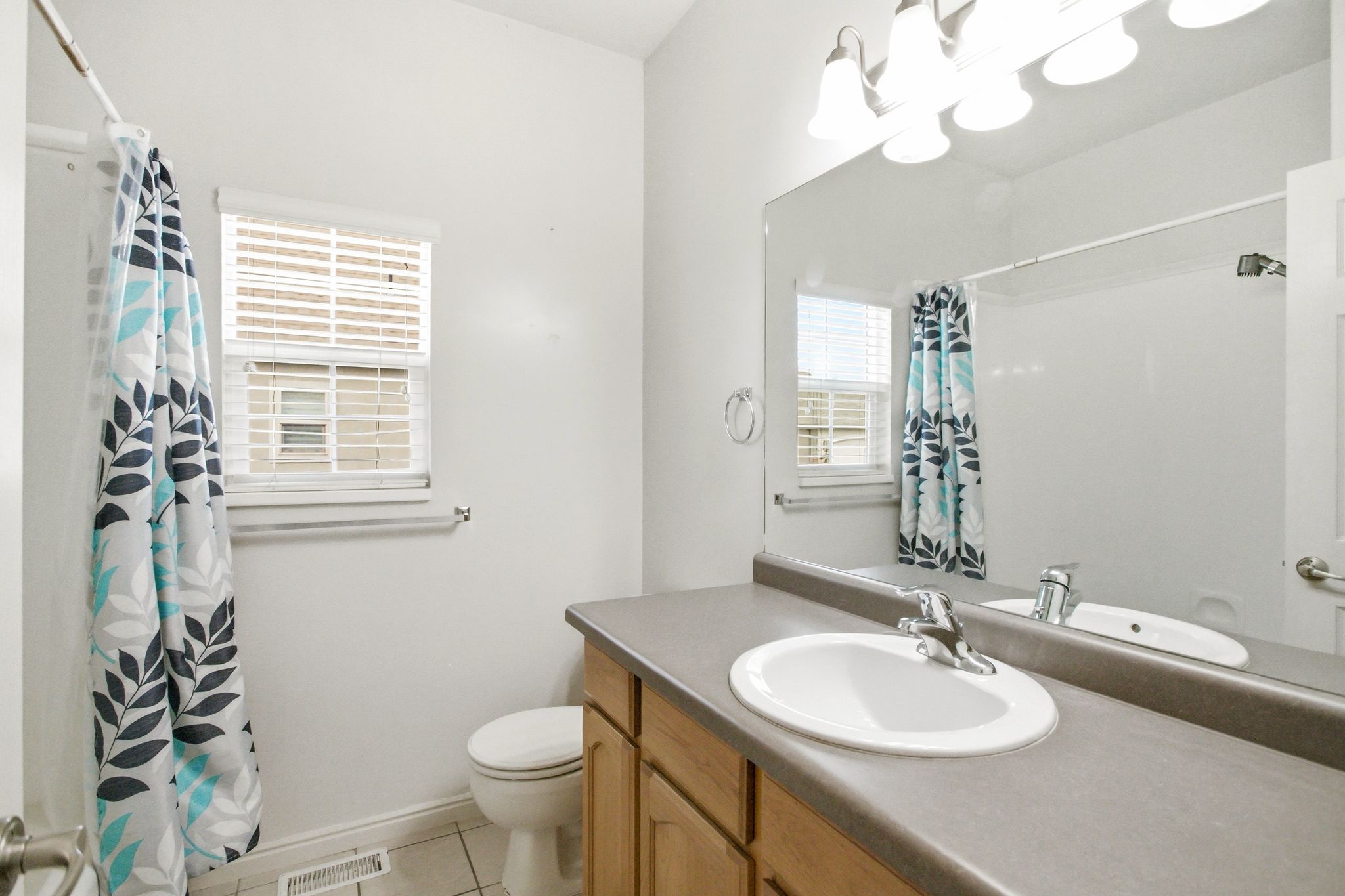 Bathroom featuring a wood-finish vanity with an integrated sink, a large wall-mounted mirror, and overhead vanity lighting