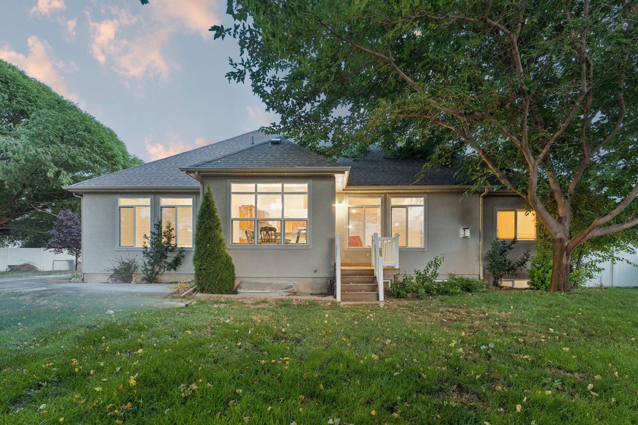 Rear exterior featuring a large grassy area, mature trees, multi-pane windows, and a raised exterior staircase