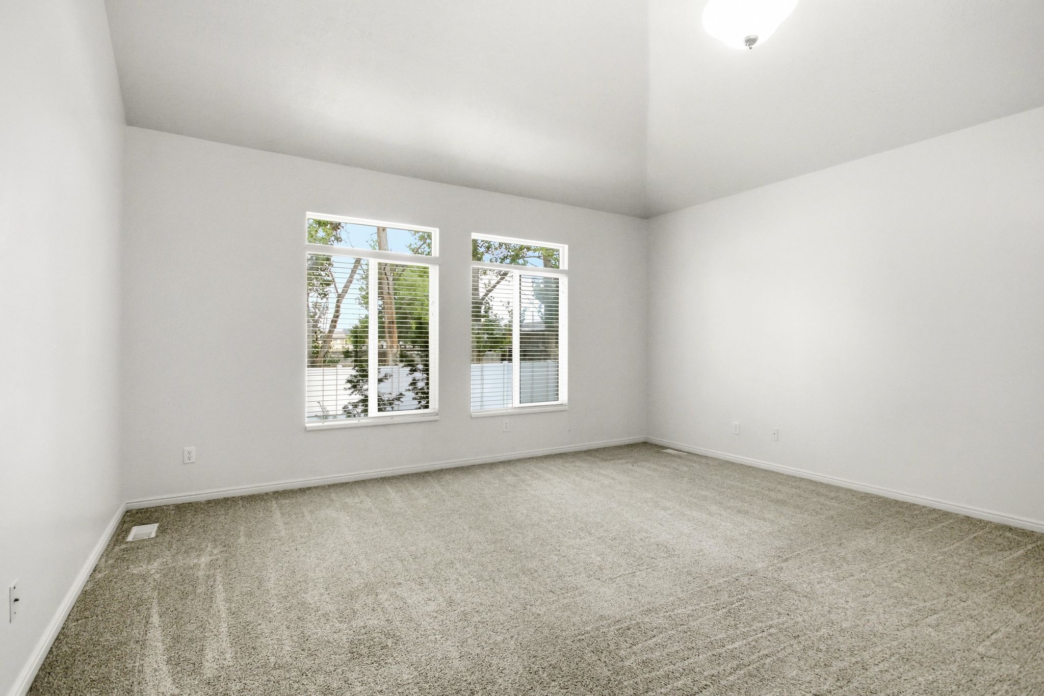 Spacious room featuring vaulted ceilings, light gray carpeting, and two large window units with blinds