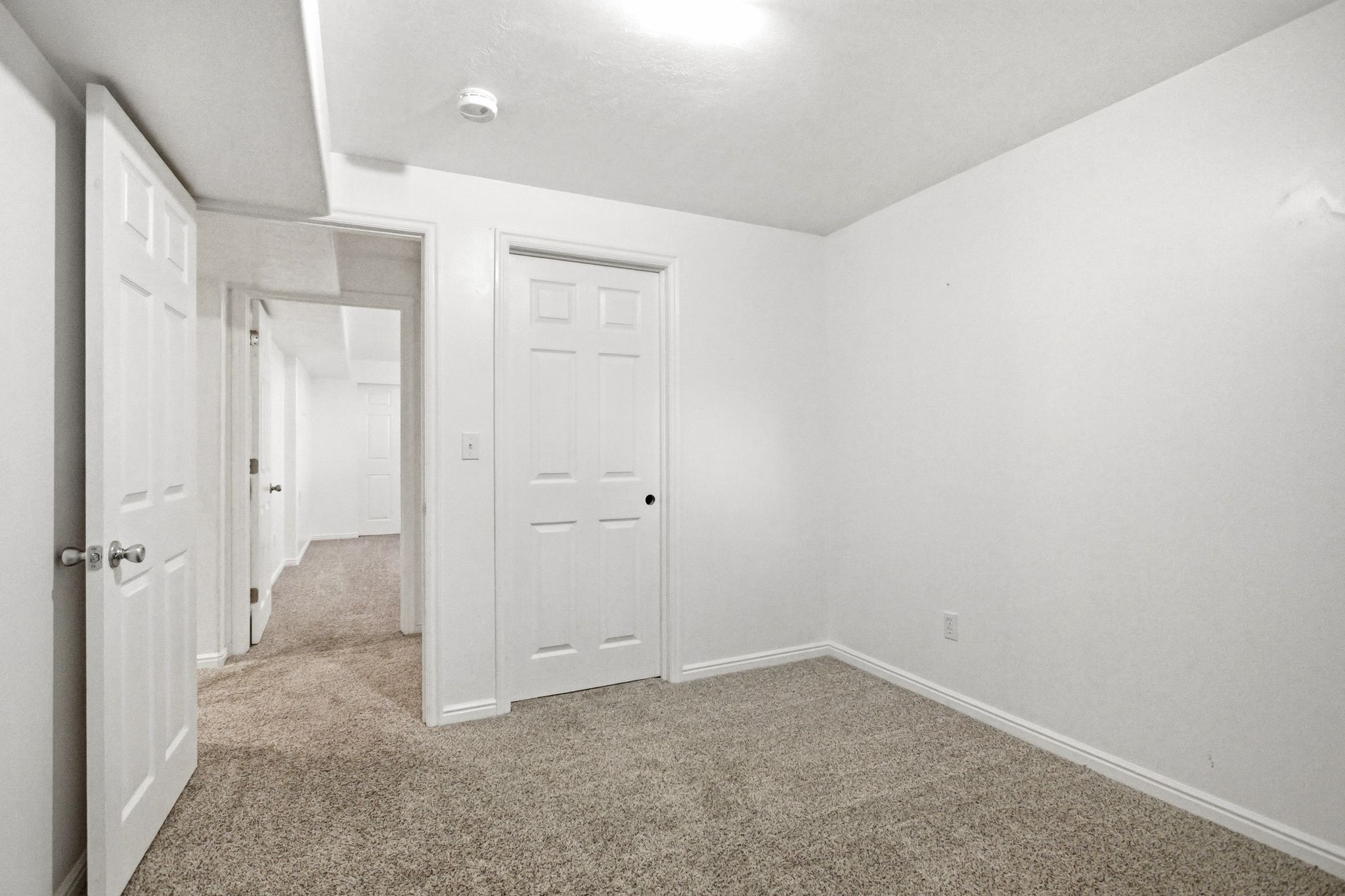 Carpeted room with white walls, white baseboards, and a six-panel door