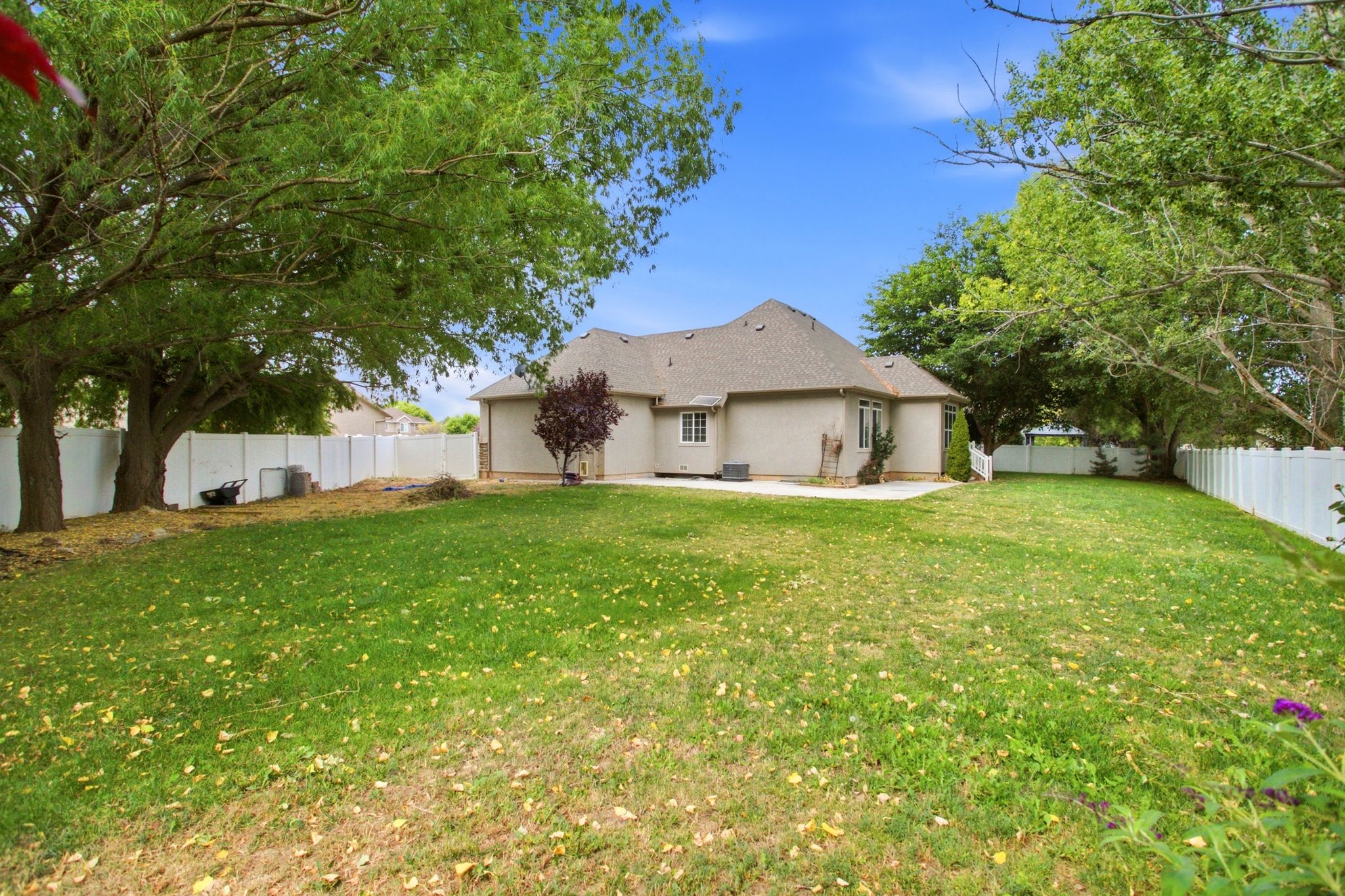 Expansive rear yard featuring a manicured lawn, mature trees, and a full privacy fence