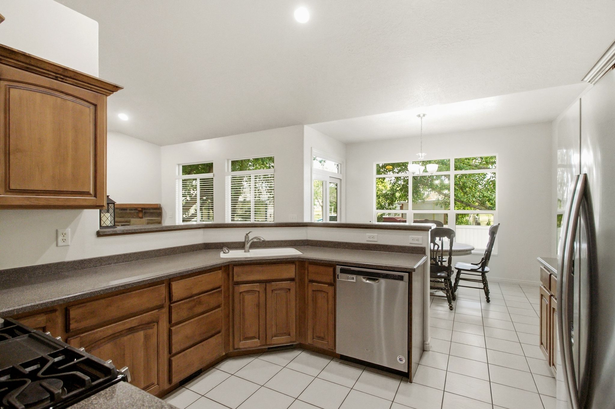 Kitchen featuring warm wood cabinetry, neutral countertops, a stainless steel dishwasher, white tile flooring, and recessed lighting