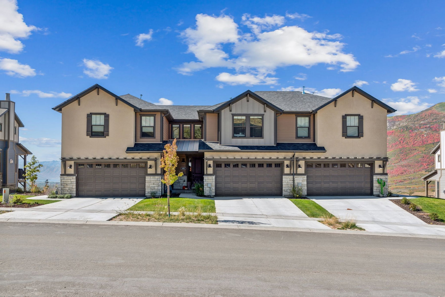 Contemporary multi-unit residence with stucco and siding exteriors, stone accents, attached garages, and a paved driveway