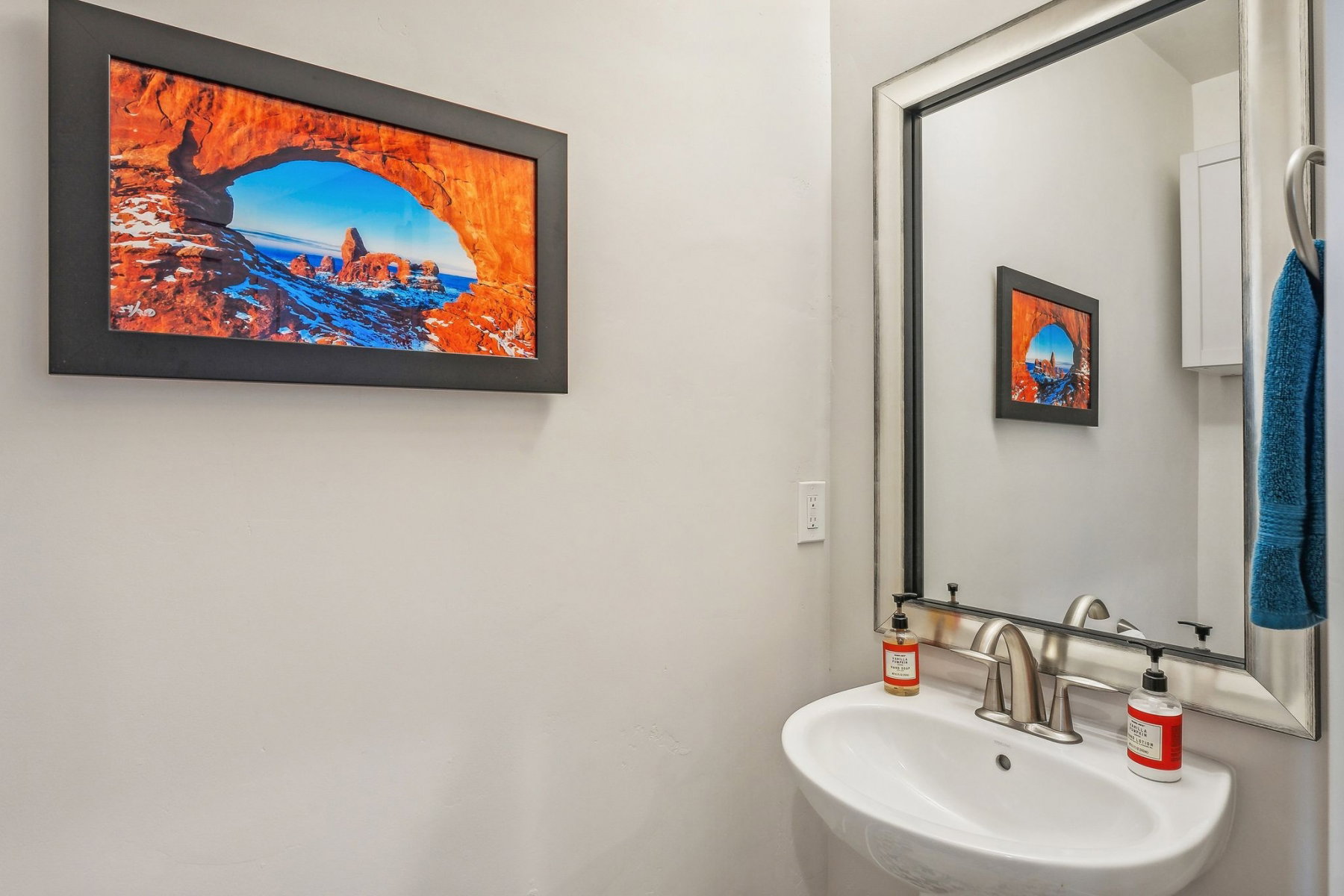 Pedestal sink with brushed nickel faucet, framed wall mirror, and wall-mounted storage cabinet
