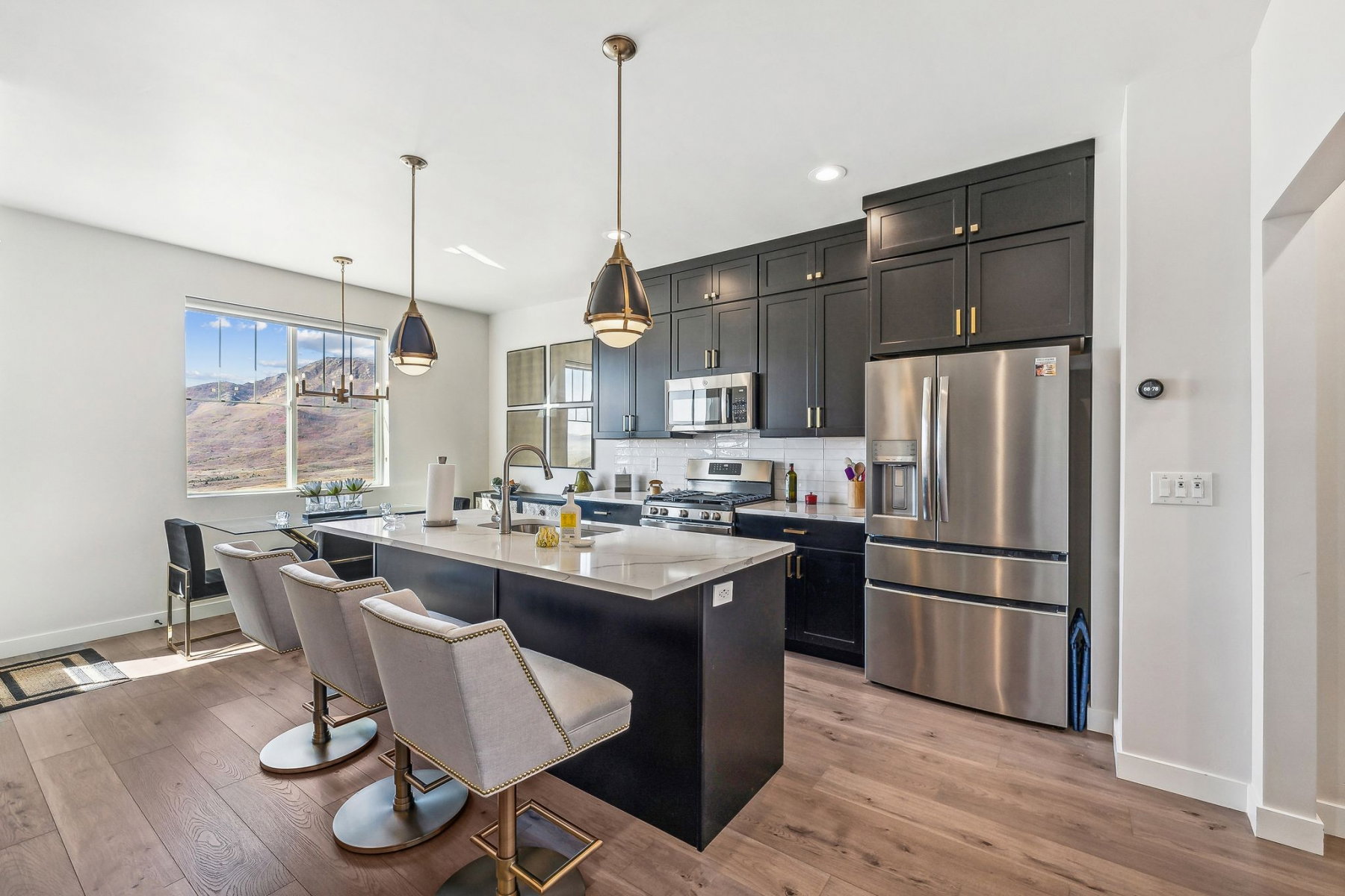 Modern kitchen featuring dark cabinetry, stainless steel appliances, a center island with bar seating, wood-finish flooring, and a large window showcasing mountain scenery