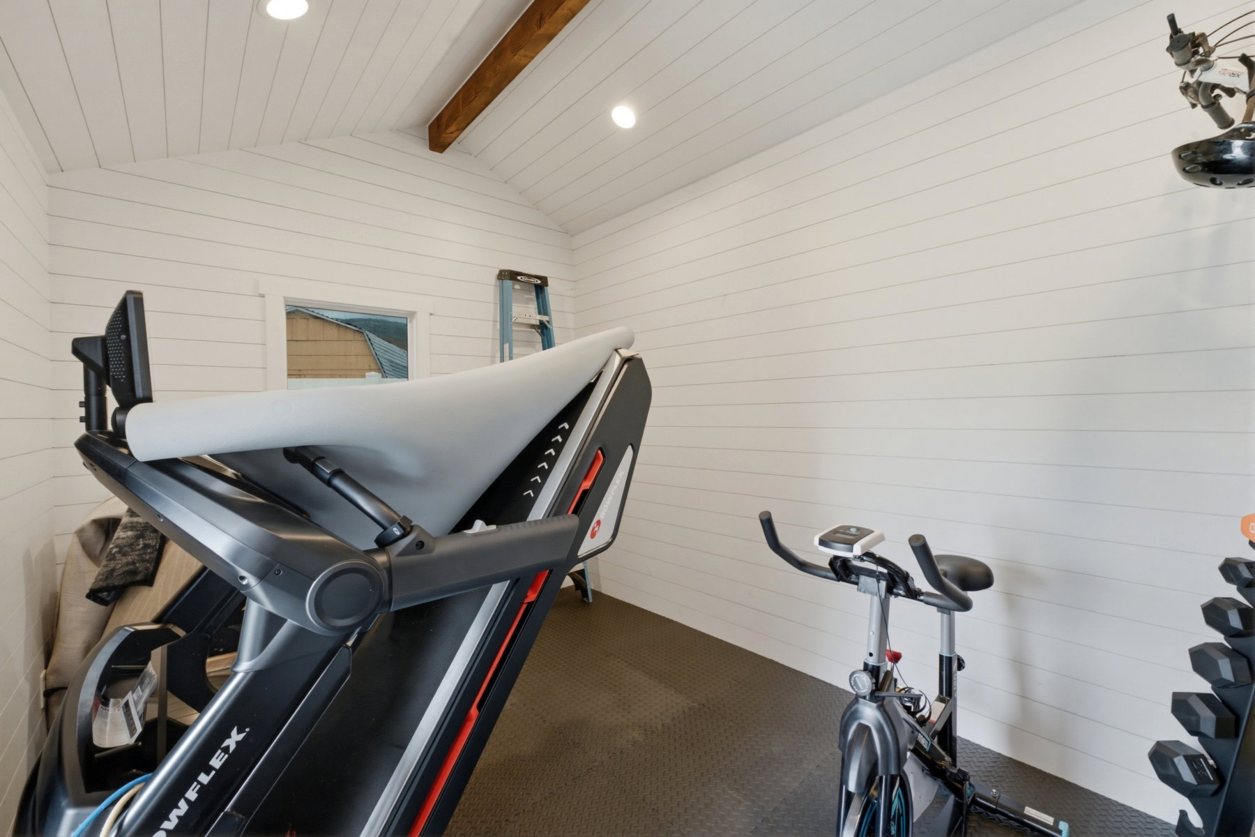 Room featuring white shiplap walls, a vaulted ceiling with exposed wood beam, recessed lighting, and dark diamond-plate textured flooring