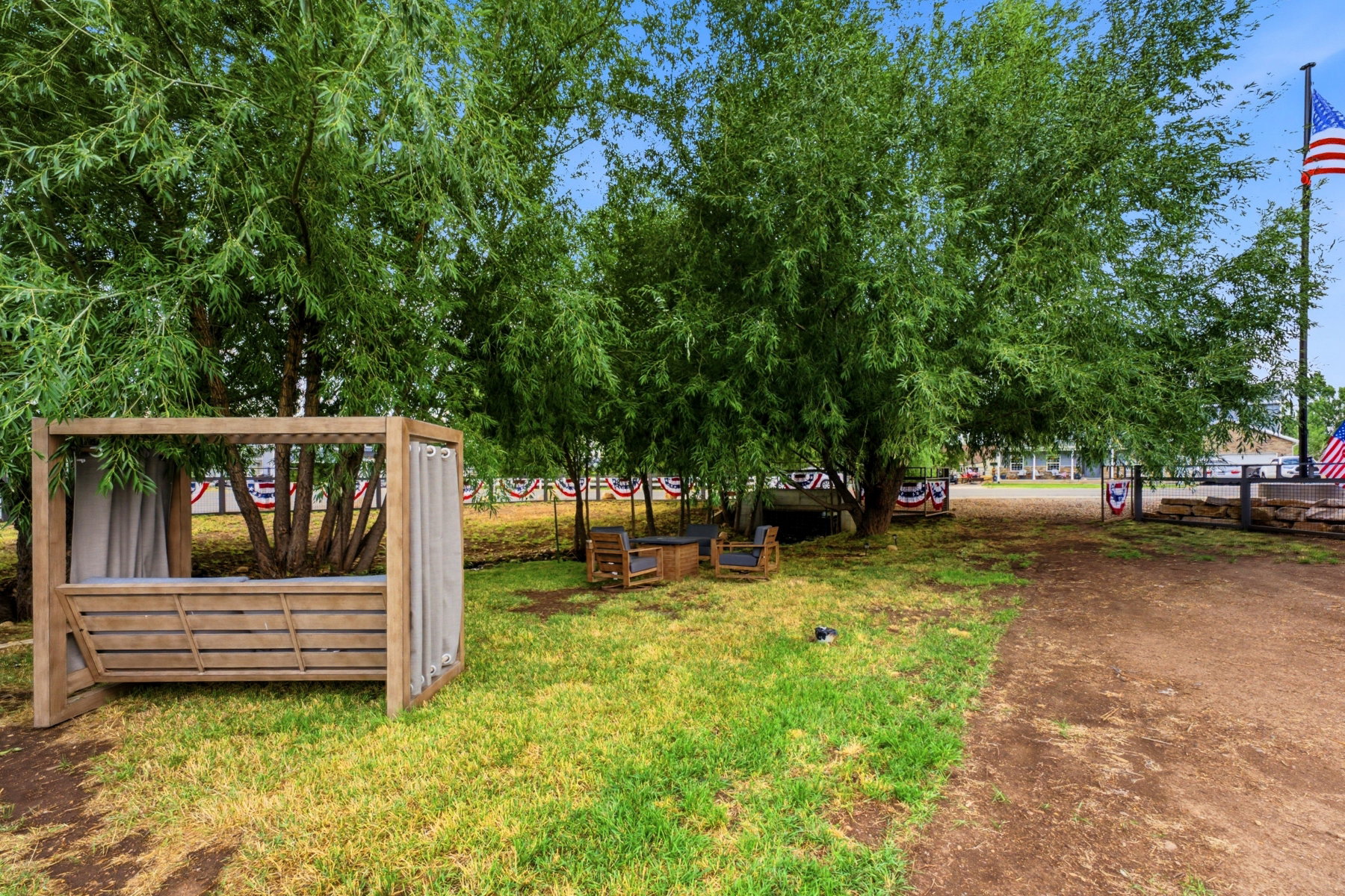 Expansive green space featuring large shade trees, a dedicated lounging cabana with privacy drapes, and a rustic ground pathway