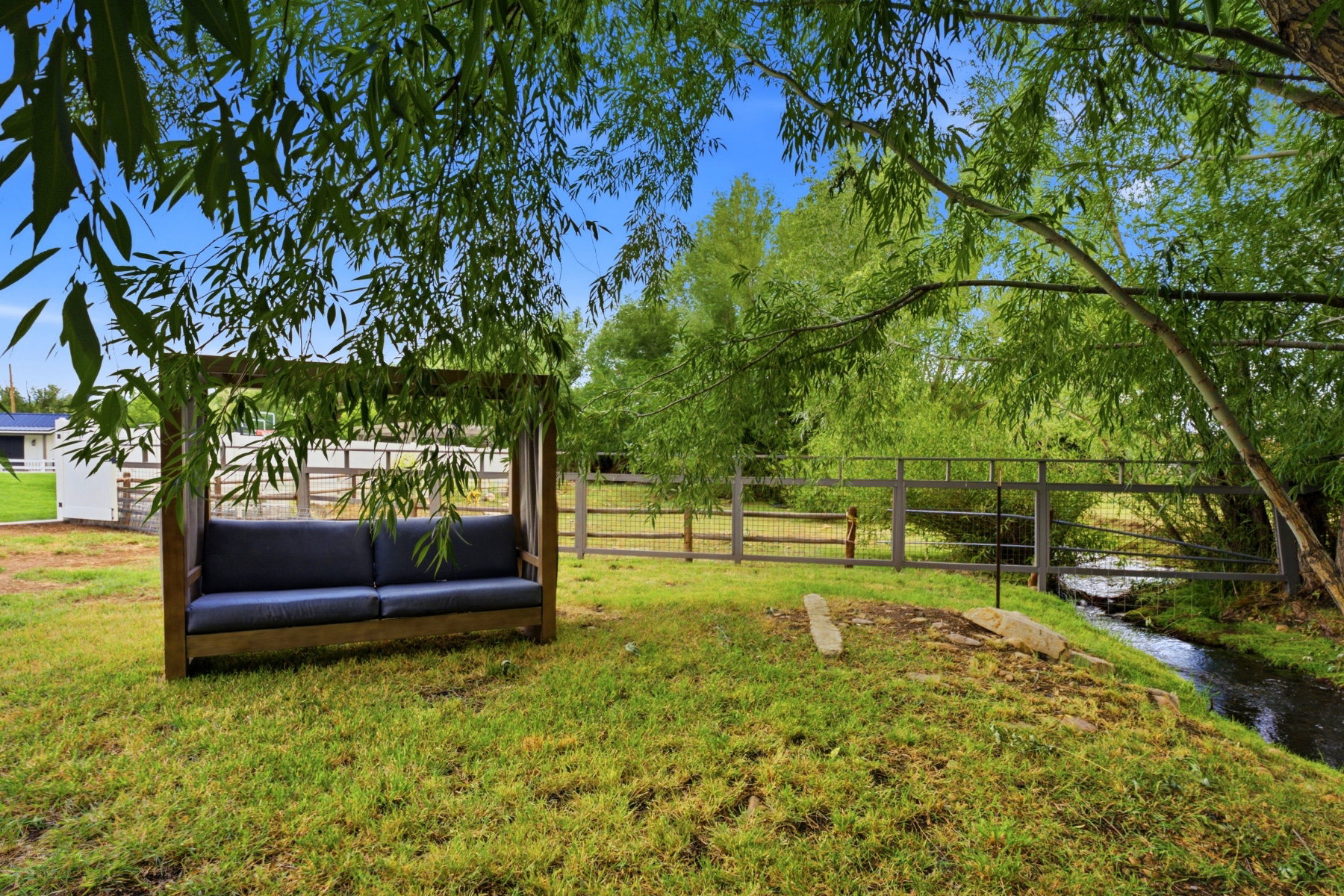 Grassy outdoor area featuring an arbor-style bench with cushions and mature trees