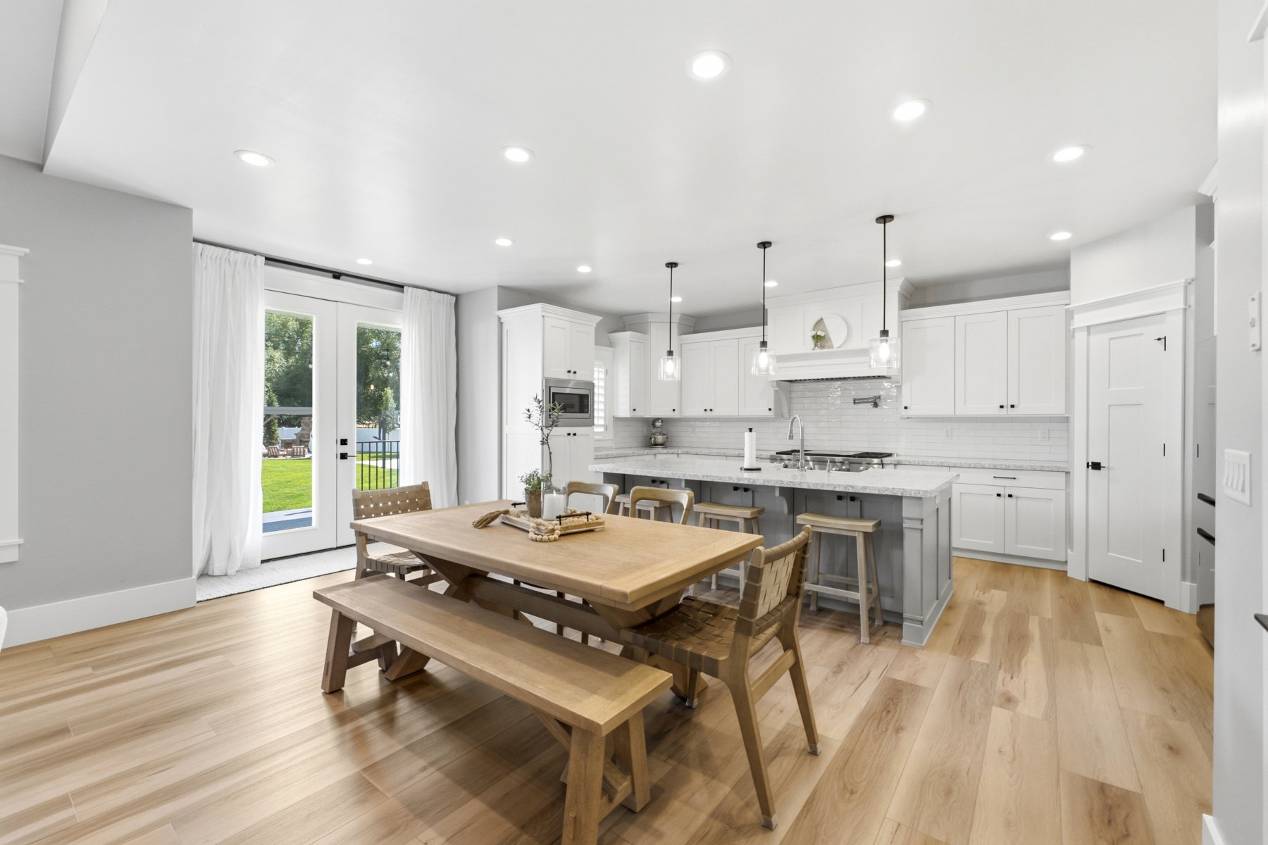 Open-concept kitchen and dining area featuring light wood-finish flooring, white cabinetry, a large kitchen island with counter seating, pendant lighting, and French doors opening to the exterior