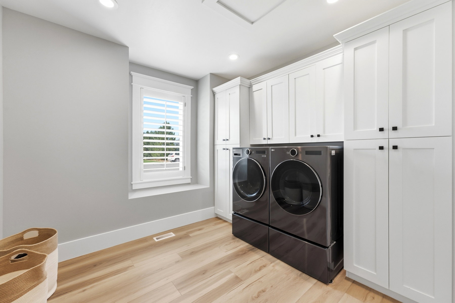 Laundry room featuring white shaker-style cabinetry, wood-finish flooring, and a window with plantation shutters