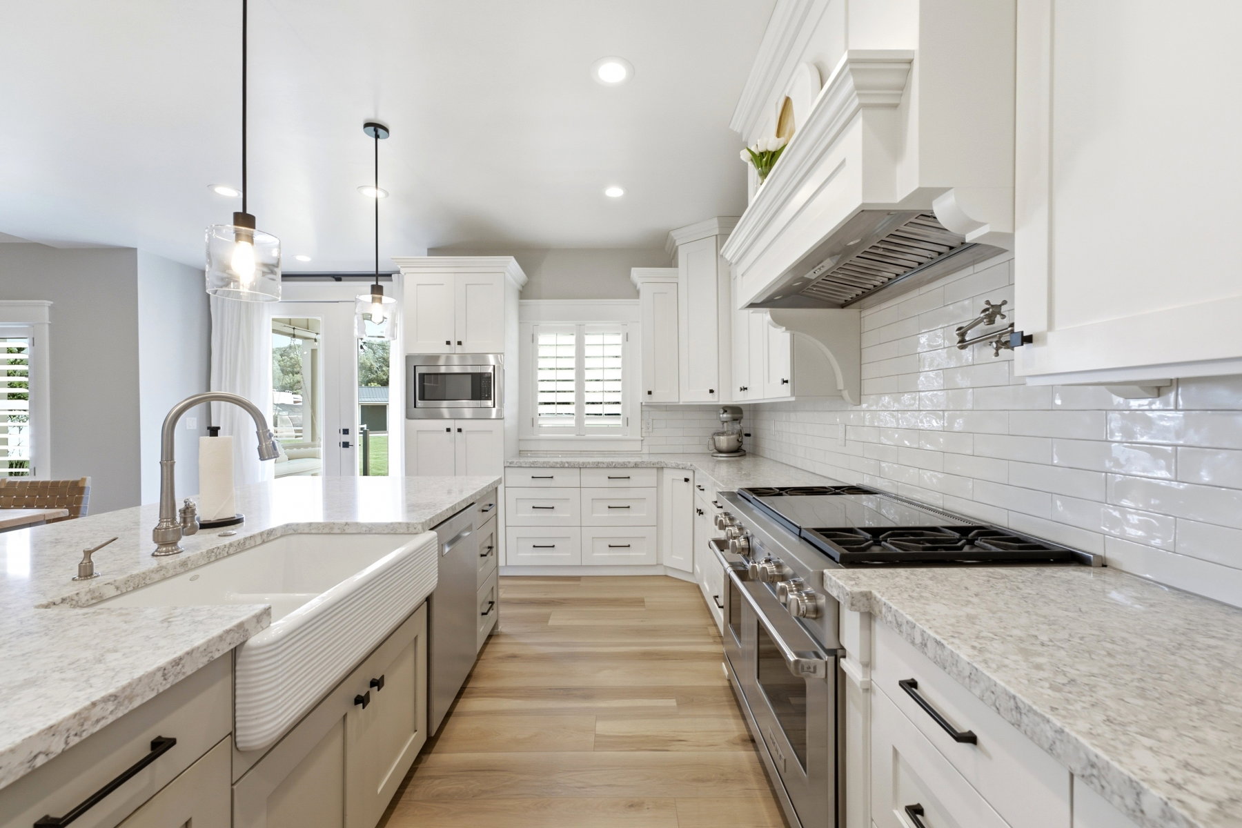Spacious kitchen featuring white shaker cabinetry, light-toned countertops, a farmhouse sink, stainless steel appliances, and wood-finish flooring