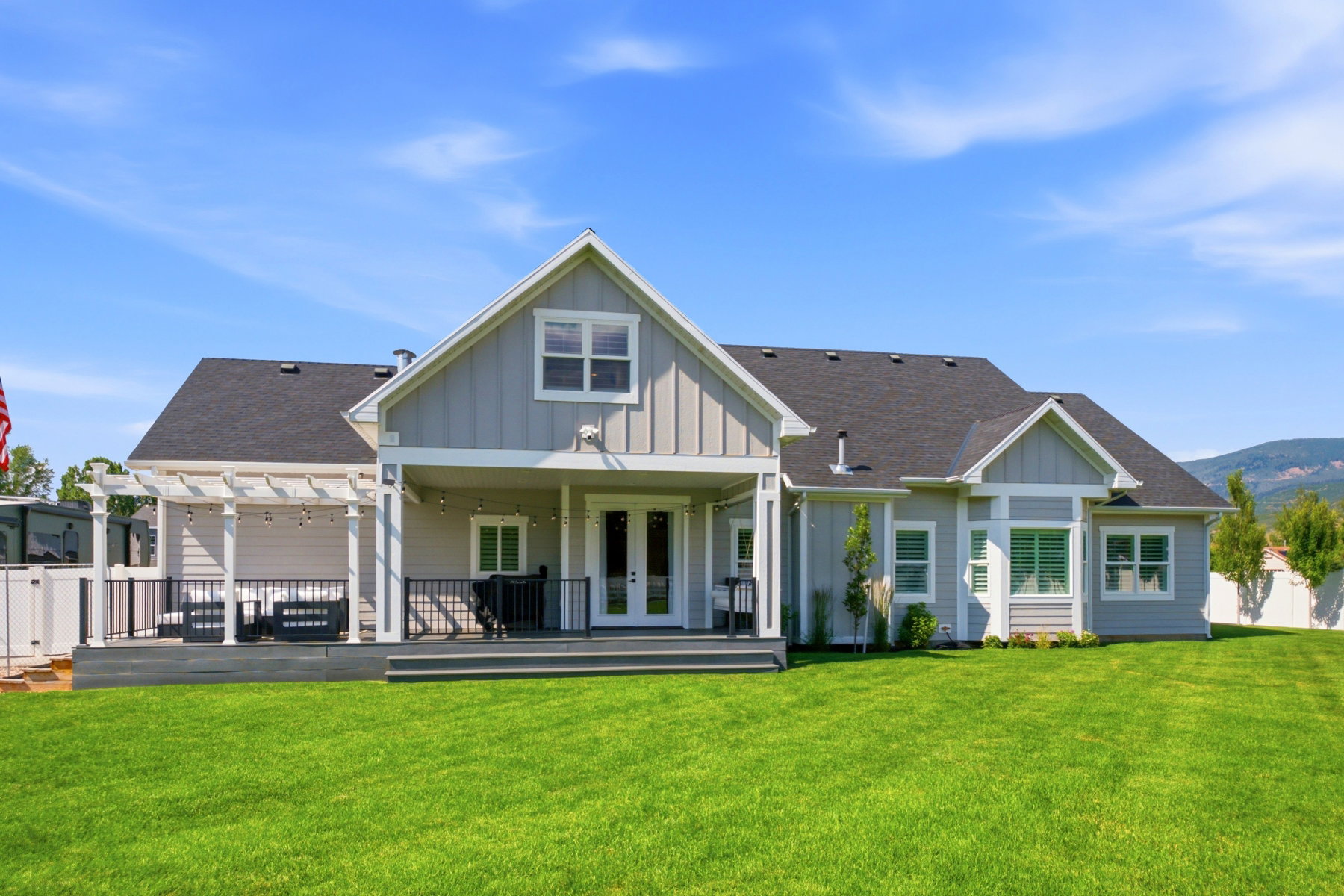 Spacious rear exterior featuring light gray siding, dark shingle roofing, and a substantial green lawn