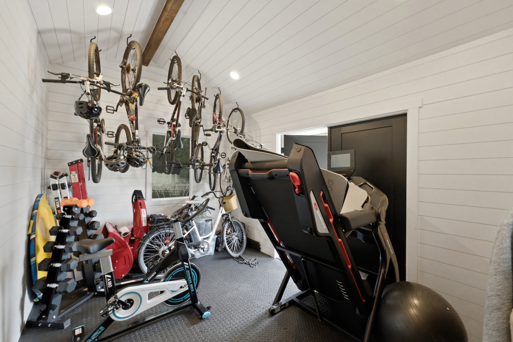 Dedicated storage room featuring shiplap walls, a vaulted ceiling with exposed wood beam, recessed lighting, and durable rubber flooring