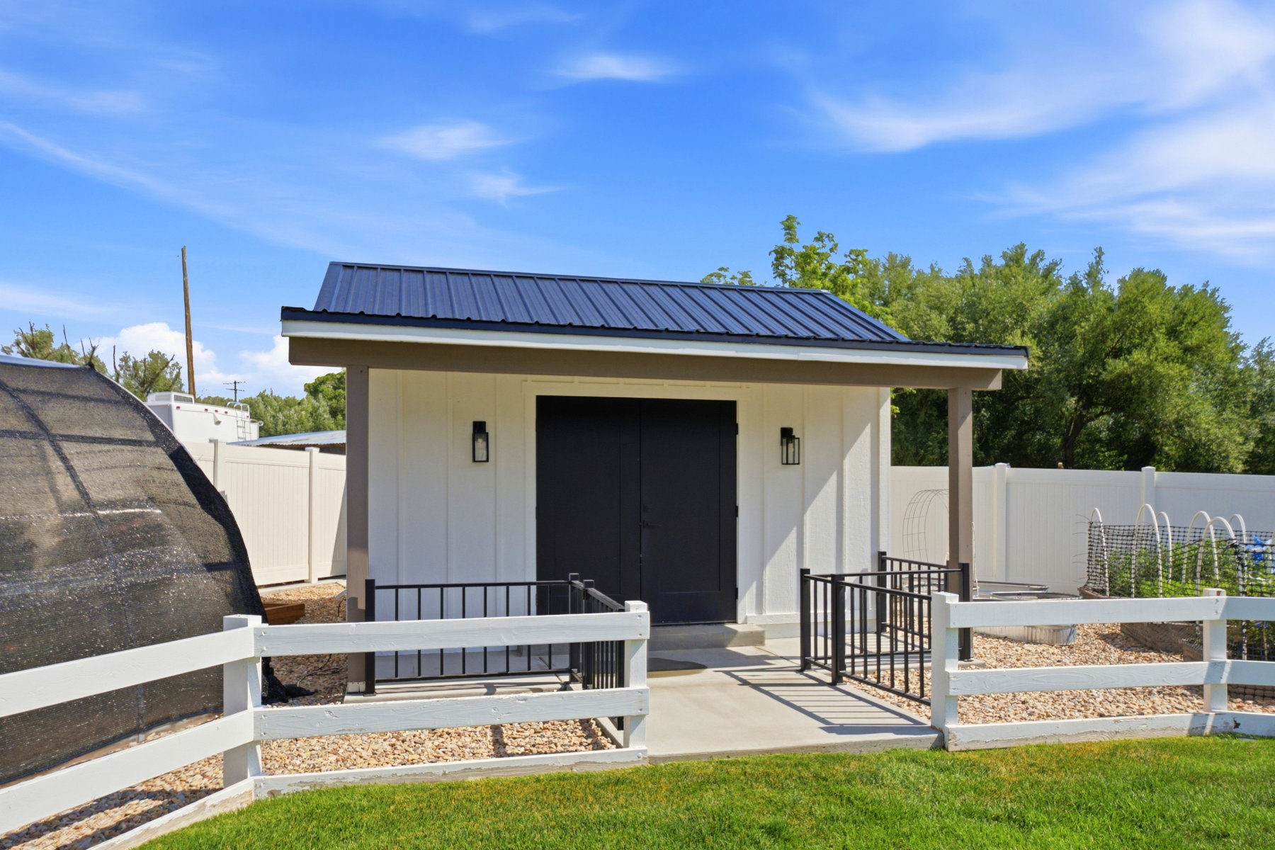 Modern detached shed with a dark metal roof, white vertical siding, and black double doors