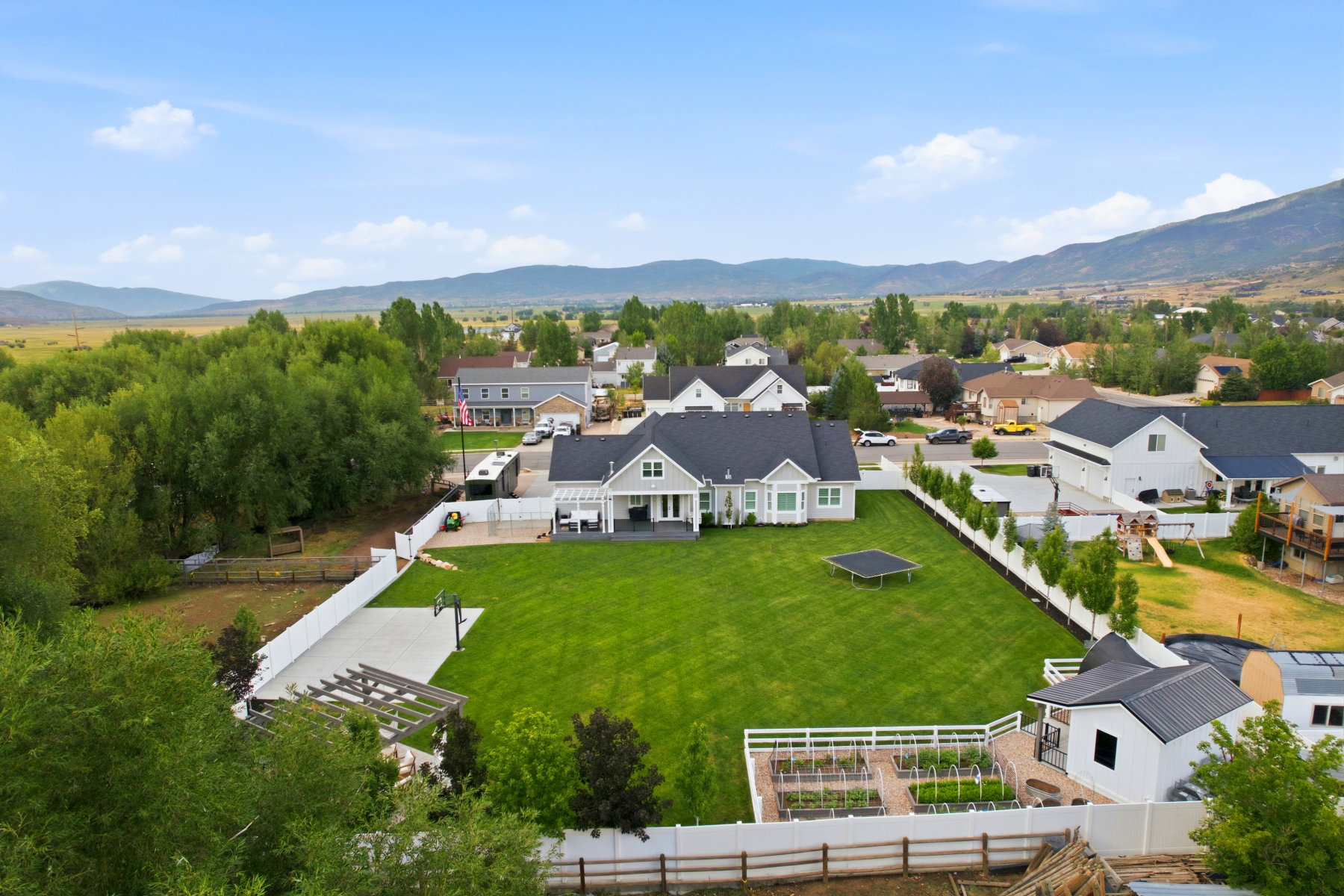 Expansive backyard featuring a large green lawn, concrete sports court with basketball hoop, pergola, and fenced garden beds