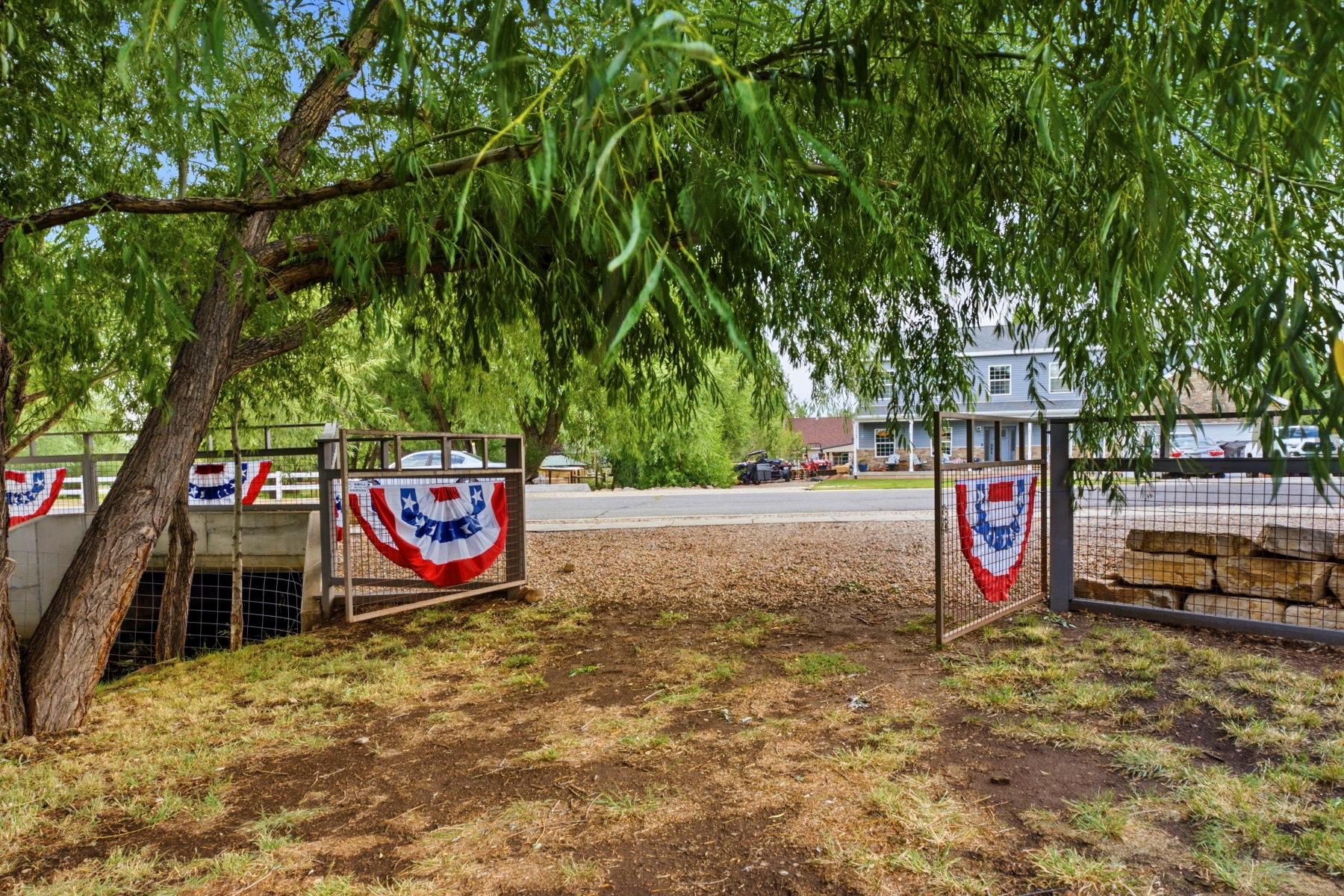 Expansive property entrance featuring mature trees and a metal gate